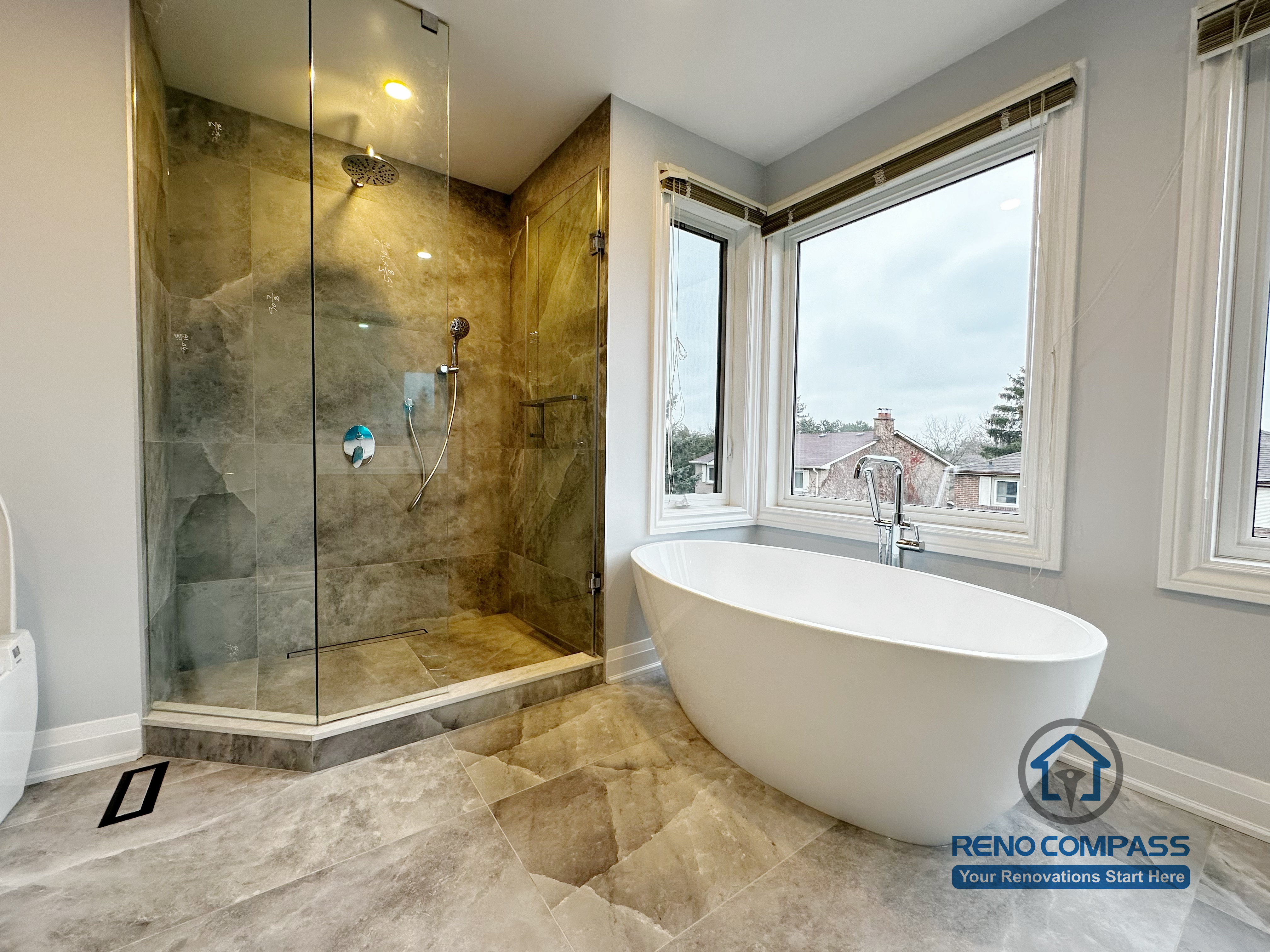 Bathroom renovation in Markham featuring a freestanding soaking tub, frameless glass shower, and large-format tile flooring. Expansive windows enhance natural light, creating a bright, spa-inspired bathroom with a clean and modern layout.