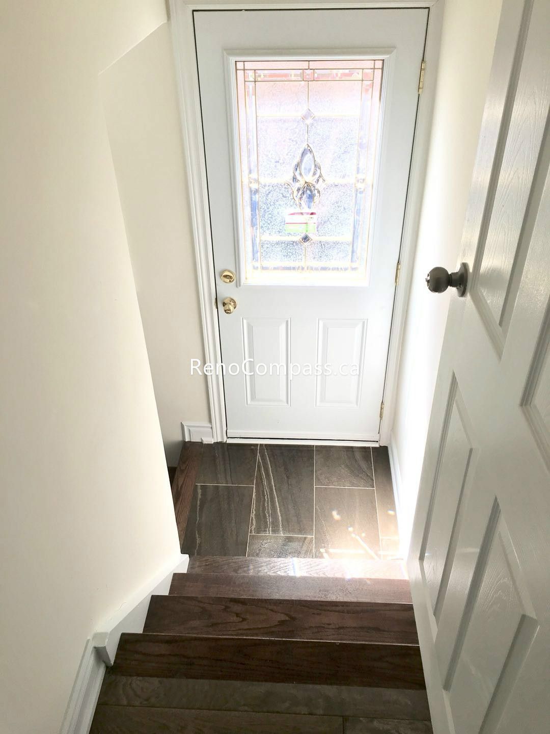 This Toronto basement renovation features a newly upgraded staircase leading to a bright basement entry with durable tile flooring and a modern exterior door with decorative glass panel. The combination of hardwood stairs and easy-maintenance flooring enhances safety, durability, and overall visual appeal. Completed by a professional Toronto renovation company, this basement entry upgrade improves functionality, lighting, and home value with quality craftsmanship.