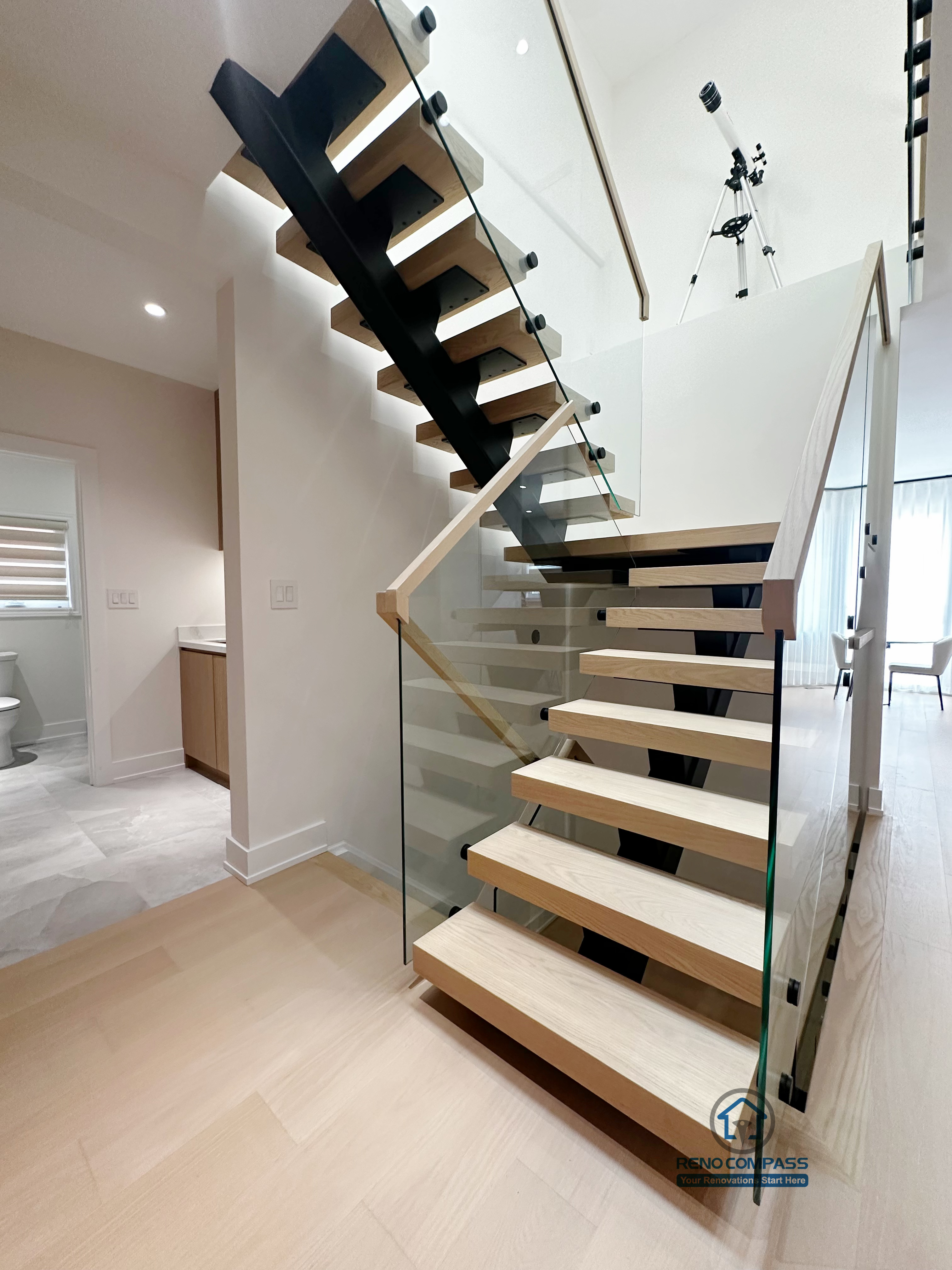 This detail view highlights the craftsmanship of the floating steel staircase, featuring solid wood treads paired with a tempered glass railing system. The design emphasizes clean lines, structural clarity, and safety, while maintaining visual openness and a seamless connection between levels.
