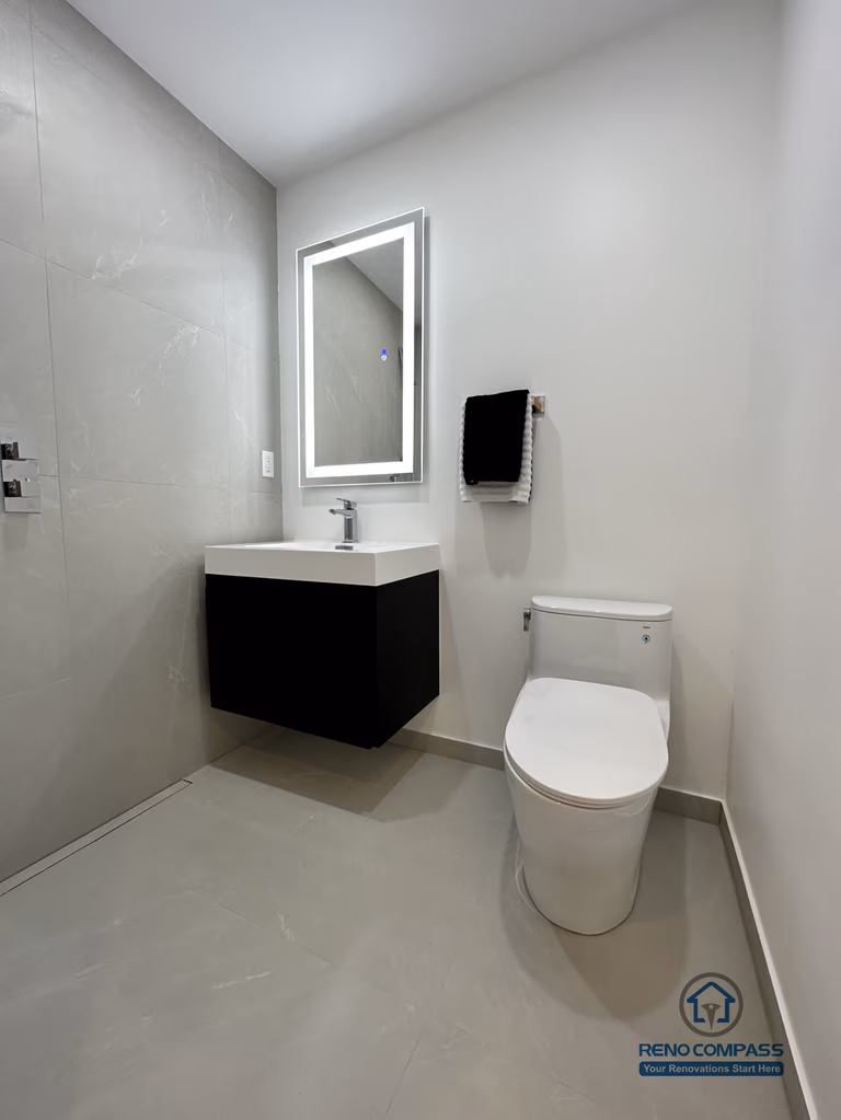 This image showcases a modern accessible pet shower bathroom renovation in Brampton, designed with a clean, barrier-free layout for ease of use. The space features large-format non-slip floor tiles, a wall-mounted floating vanity, an LED backlit mirror, and a compact toilet configuration to maximize maneuverability. The open shower area allows safe and comfortable bathing for pets while remaining fully accessible for homeowners. This type of thoughtful, functional design is ideal for aging-in-place and pet-friendly homes, completed by a professional Toronto Renovation Company with experience in accessibility-focused bathroom solutions.