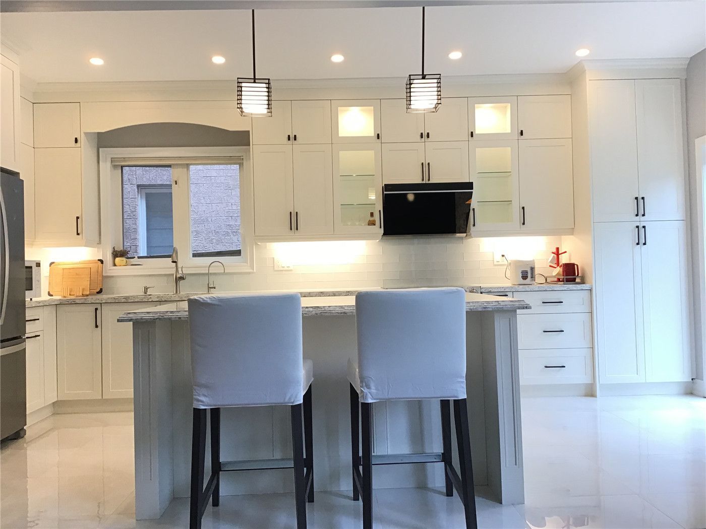 This Richmond Hill interior renovation features a bright open-concept kitchen centered around a large quartz island with seating. The space is designed with full-height custom cabinetry, clean white finishes, and modern pendant lighting that enhances both functionality and visual appeal. The symmetrical layout, under-cabinet lighting, and efficient workflow create a welcoming and practical environment for everyday living. Completed by a professional Toronto renovation company, this project reflects a refined and timeless kitchen design.