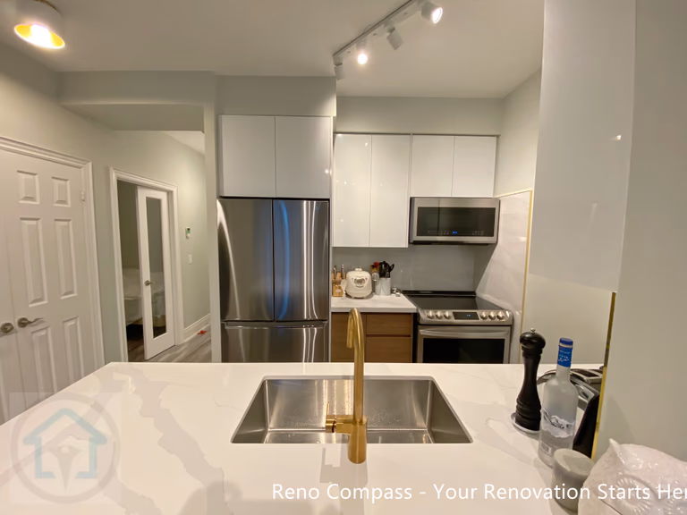 This North York condo kitchen renovation highlights a clean, functional layout with a quartz countertop island, undermount sink, and brushed brass faucet as a subtle focal point. Glossy white cabinetry, stainless steel appliances, and track lighting enhance brightness while maximizing space efficiency. The updated design improves workflow, storage, and daily usability, making the kitchen well-suited for modern condo living and long-term property value.