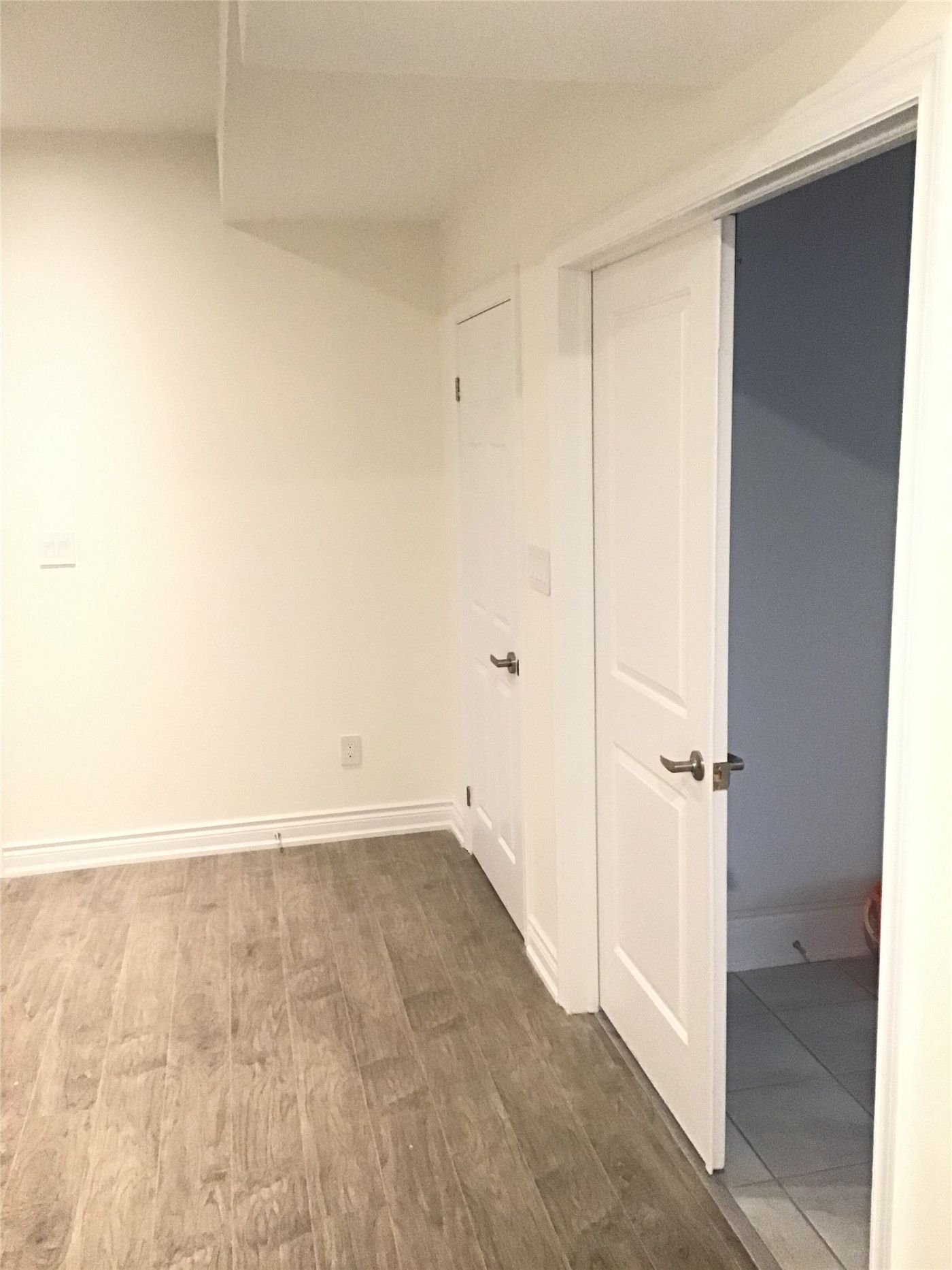 This Aurora interior renovation features a clean and modern basement hallway with newly installed white doors, wood-look vinyl flooring, and a bright neutral color palette. The space is designed for functionality and flow, connecting different rooms while maintaining a sleek and contemporary finish.