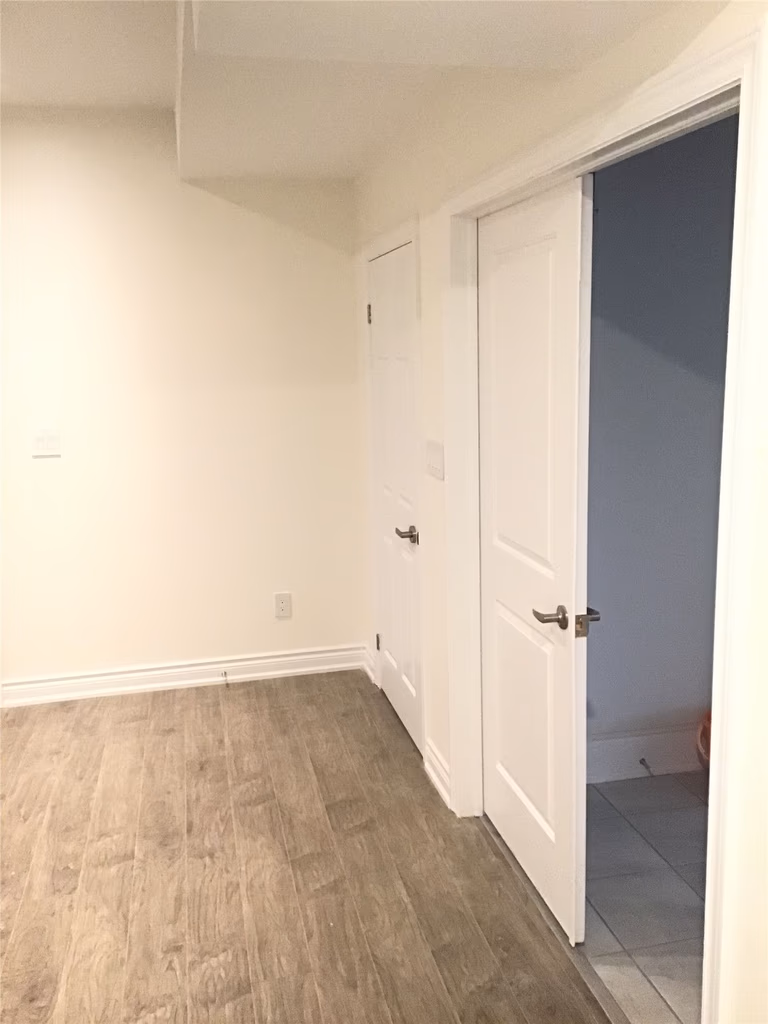This Aurora interior renovation features a clean and modern basement hallway with newly installed white doors, wood-look vinyl flooring, and a bright neutral color palette. The space is designed for functionality and flow, connecting different rooms while maintaining a sleek and contemporary finish.