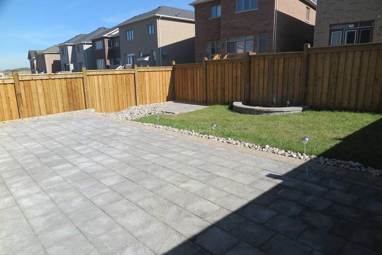 Spacious backyard interlocking patio completed in Aurora featuring modern grey stone pavers, clean linear layout, and decorative gravel border along the wooden fence. This professional landscaping and paving project creates a durable, low-maintenance outdoor space ideal for entertaining and everyday use. Installed by Reno Compass Inc., a trusted Toronto renovation and landscaping contractor serving Aurora and surrounding GTA areas.
