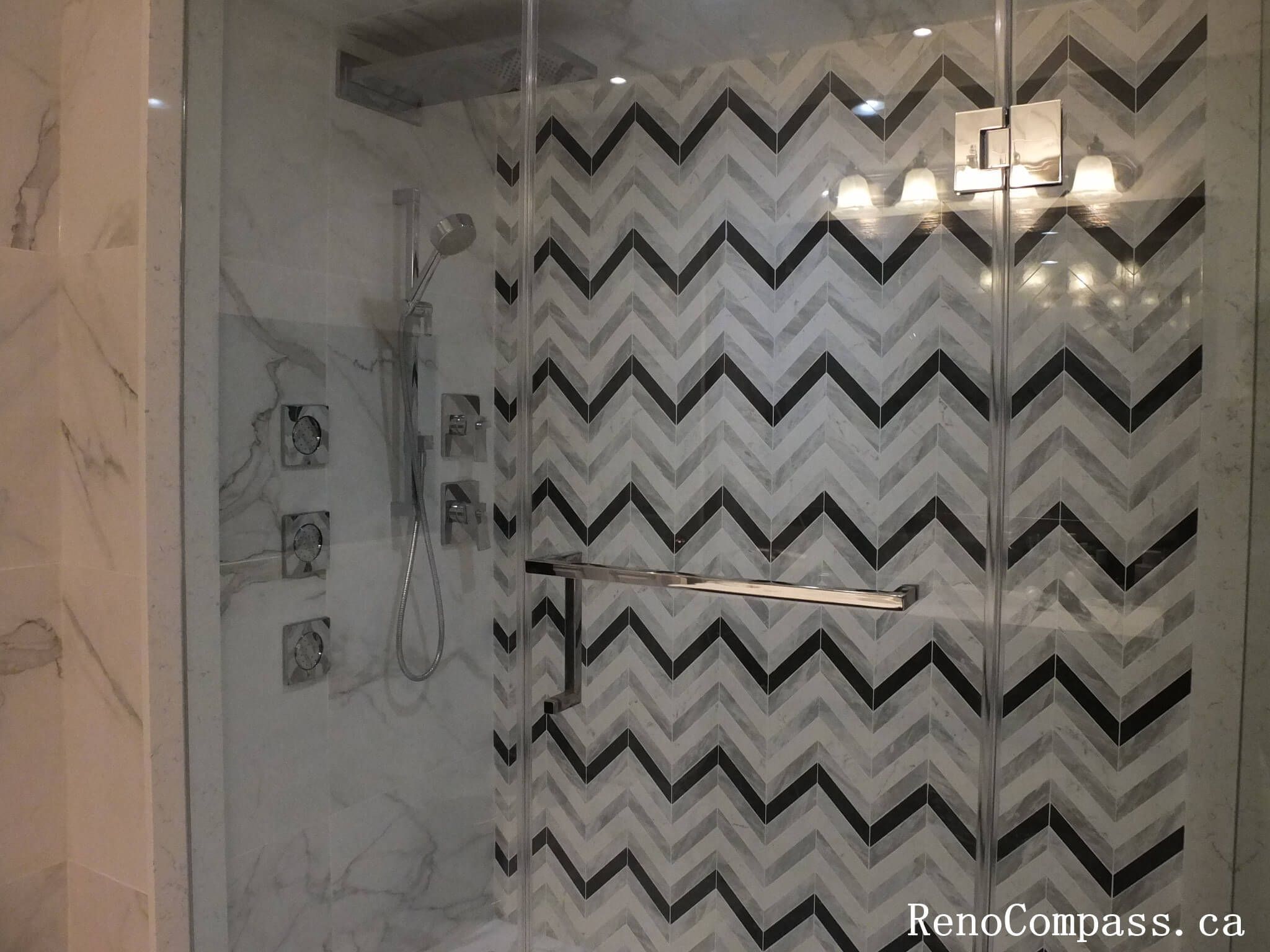Frameless glass shower with a black and white chevron mosaic accent wall and luxury chrome body jets.
