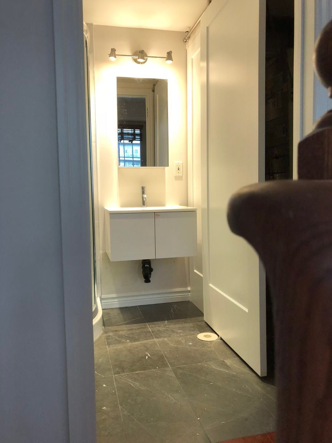 This Toronto bathroom renovation features a sleek floating vanity with integrated sink, LED backlit mirror, and modern wall lighting. Dark floor tiles contrast with clean white cabinetry to create a contemporary and functional space. The upgraded layout improves storage, lighting, and daily usability, delivering a bright and modern bathroom design ideal for urban living.