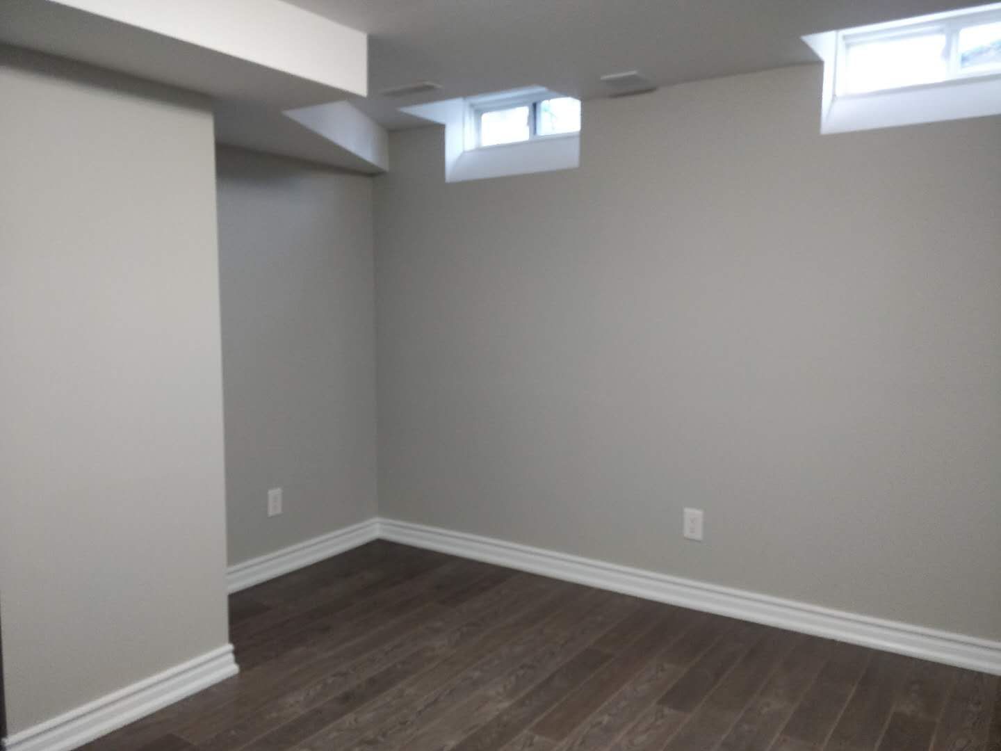 This Scarborough basement renovation showcases a finished room with modern hardwood flooring, freshly painted walls, and built-in closet space with sliding mirrored doors. The clean design and neutral color palette create a bright and practical basement bedroom or multi-purpose living area, completed by a professional Toronto renovation company.