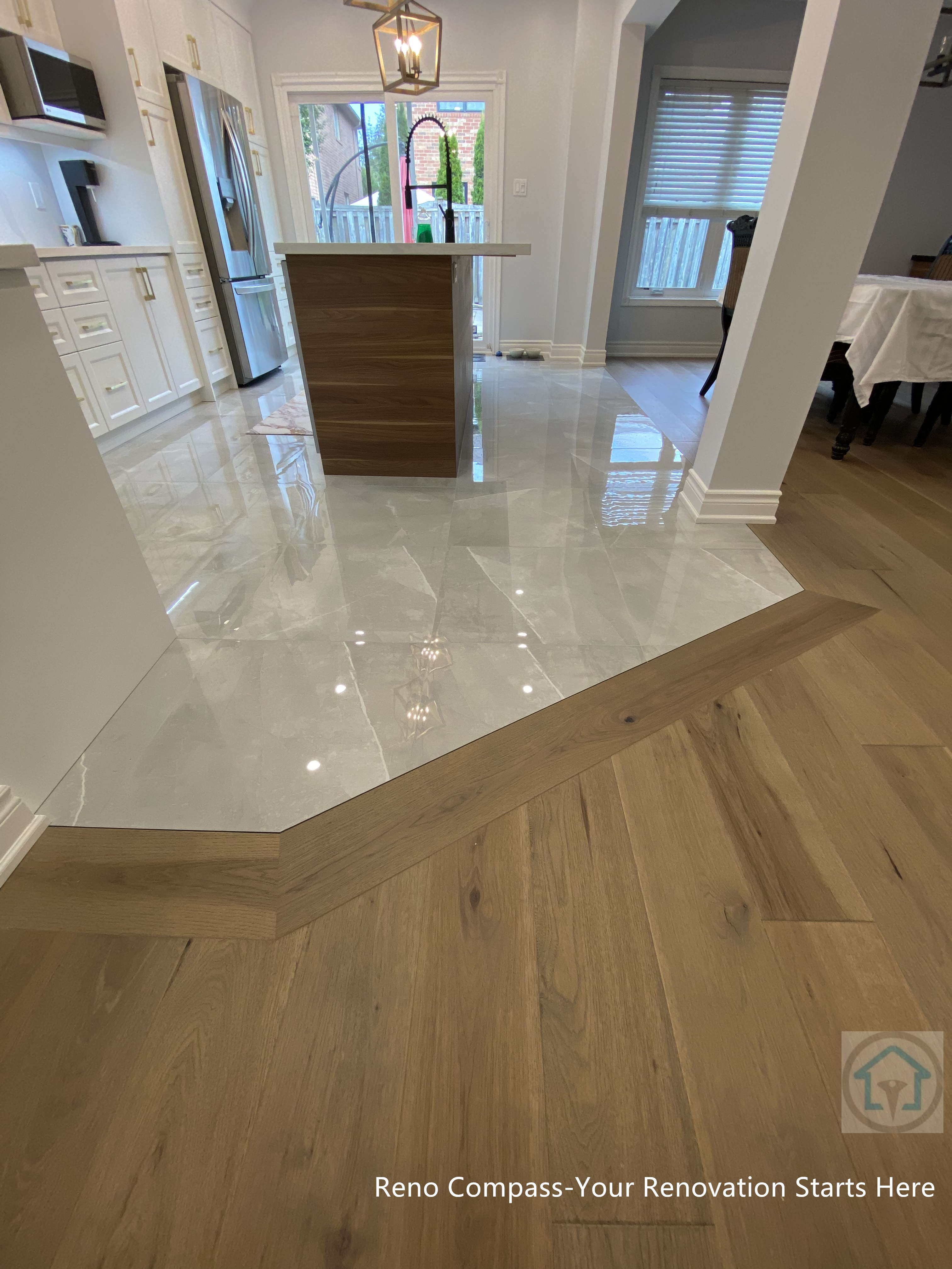 Interior renovation in Newmarket showcasing a seamless transition between large-format polished tile flooring and engineered hardwood floors. The angled transition detail creates a clean visual boundary between the kitchen and living areas while maintaining flow in the open-concept layout. The central kitchen island anchors the space, combining modern finishes with practical zoning by a Toronto renovation company specializing in full home interior renovations.