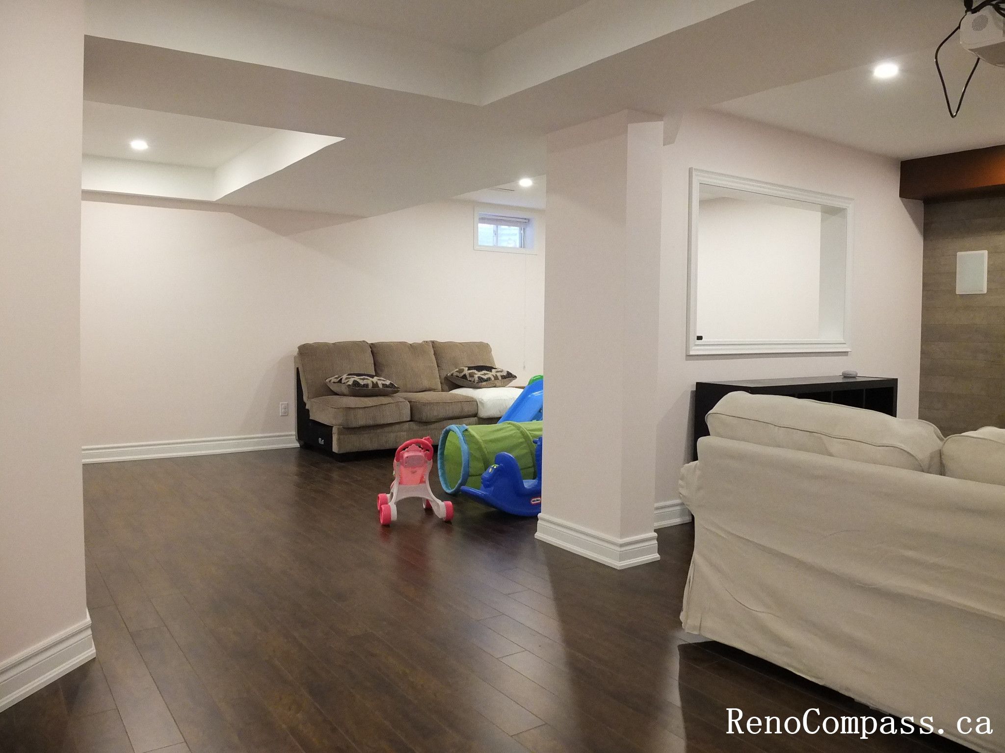 Spacious basement living area renovation in Newmarket featuring an open-concept layout, dark engineered hardwood flooring, recessed pot lights, support columns, and a comfortable family seating zone. Designed and completed by a trusted Toronto Renovation Company to create a bright and functional multi-purpose lower level.