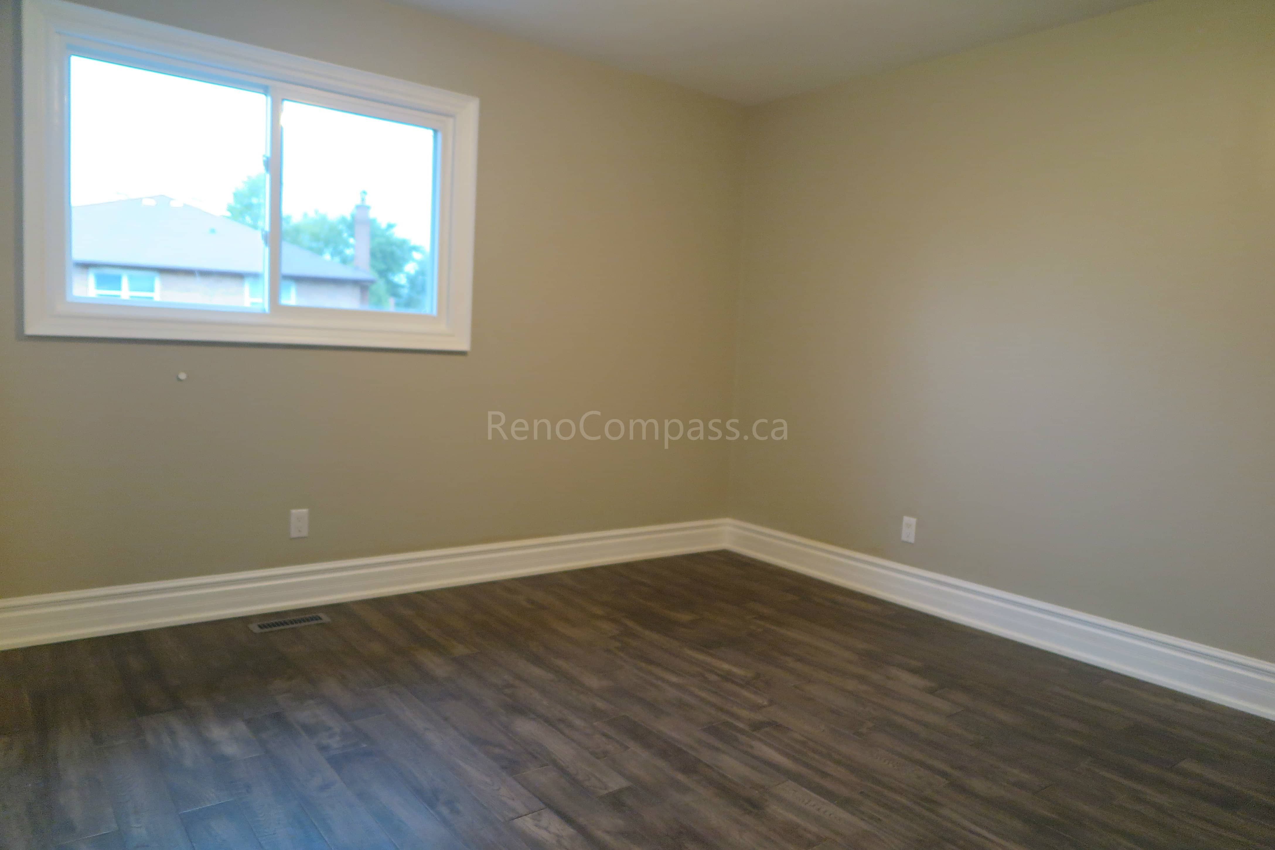 This Markham interior renovation features a refreshed bedroom with newly installed dark hardwood flooring, neutral modern wall colors, and updated trim details. Large windows provide natural light, creating a bright and comfortable living space suitable for family use or guest accommodation. Completed by Reno Compass, a professional renovation contractor specializing in full home interior renovations and flooring installation across Markham and the Greater Toronto Area.