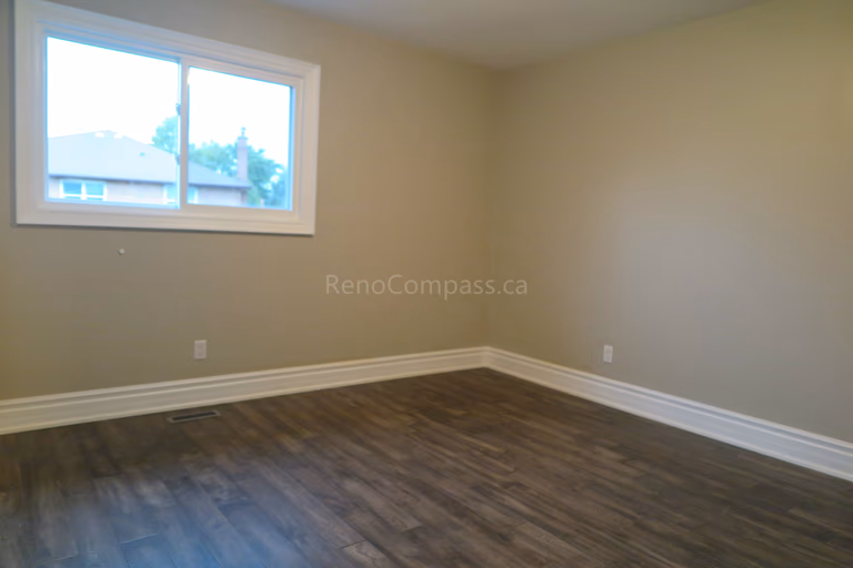 This Markham interior renovation features a refreshed bedroom with newly installed dark hardwood flooring, neutral modern wall colors, and updated trim details. Large windows provide natural light, creating a bright and comfortable living space suitable for family use or guest accommodation. Completed by Reno Compass, a professional renovation contractor specializing in full home interior renovations and flooring installation across Markham and the Greater Toronto Area.