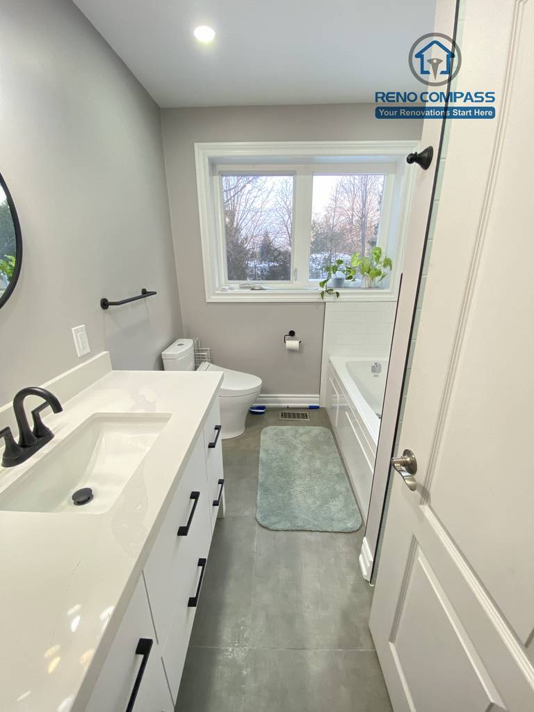 This North York bathroom renovation highlights a modern double-drawer vanity paired with a quartz countertop, matte black faucet, and matching hardware. The round mirror and wall-mounted lighting enhance both functionality and visual balance, creating a clean and efficient bathroom space completed by a Toronto renovation company focused on quality materials and precise installation.