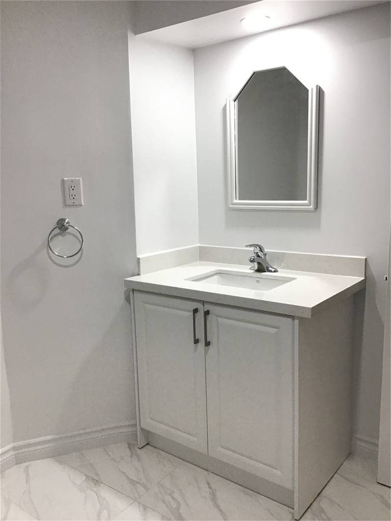 This Whitby basement renovation includes a sleek and modern bathroom vanity installation with a white cabinet, quartz-style countertop, and contemporary mirror design. The marble-look floor tiles add elegance while maintaining durability and easy maintenance. Clean lines, neutral tones, and professional plumbing installation create a bright and functional basement bathroom space that enhances both comfort and home value.