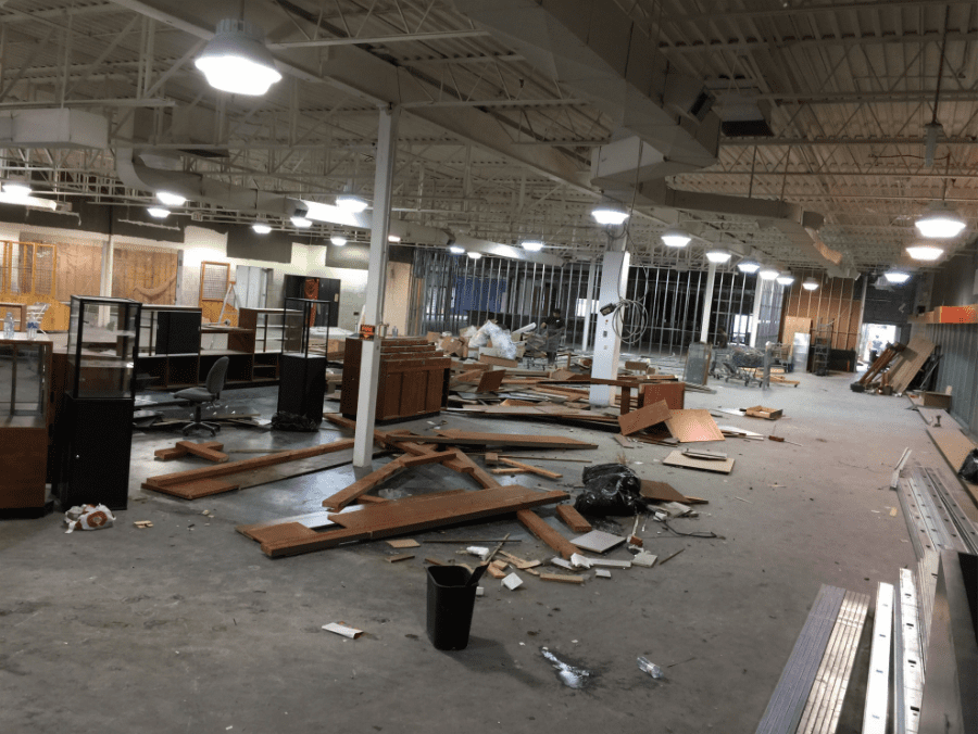 This image captures the construction phase of an outdoor retail store renovation, featuring structural ceiling framing, custom wood wall installation, and lighting preparation. The team is installing overhead framing and wood panel backdrops to support future retail displays and shelving systems. Reno Compass Inc. ensures precise craftsmanship and proper structural alignment during every stage of the commercial renovation process, building a durable and well-designed retail environment from the ground up.