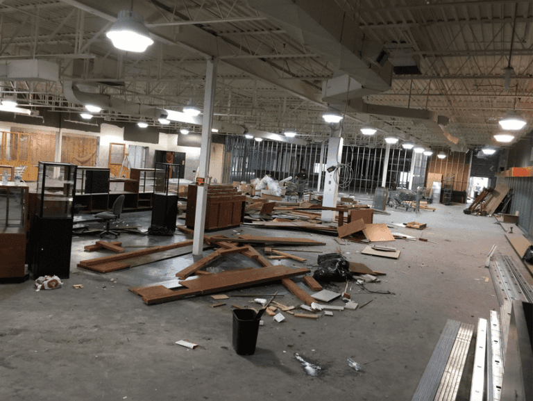 This image captures the construction phase of an outdoor retail store renovation, featuring structural ceiling framing, custom wood wall installation, and lighting preparation. The team is installing overhead framing and wood panel backdrops to support future retail displays and shelving systems. Reno Compass Inc. ensures precise craftsmanship and proper structural alignment during every stage of the commercial renovation process, building a durable and well-designed retail environment from the ground up.