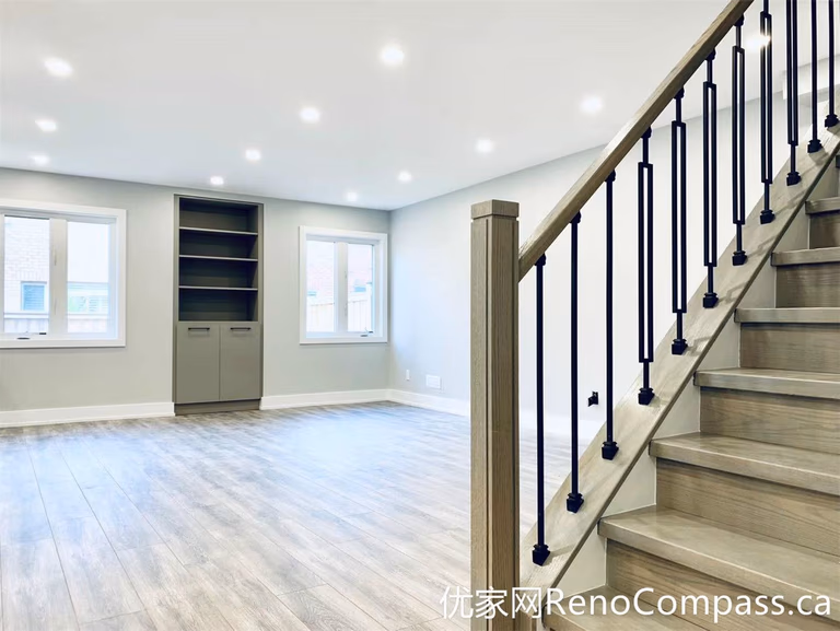 This Markham full home renovation features a bright open-concept basement with wood-look flooring, recessed pot lights, and a custom staircase with black metal railings. The clean layout and built-in shelving create a functional and inviting living area, ideal for family use or additional entertainment space.