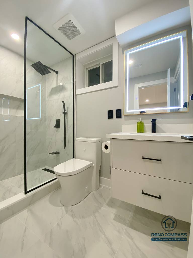 This Aurora basement renovation features a modern full bathroom with a glass-enclosed shower, marble-look wall and floor tiles, a floating vanity, and an LED-lit mirror. The compact layout is designed for efficiency and comfort, combining clean lines with durable finishes suitable for basement use. Completed by a Toronto renovation company, this basement bathroom renovation reflects thoughtful space planning and contemporary bathroom design standards.