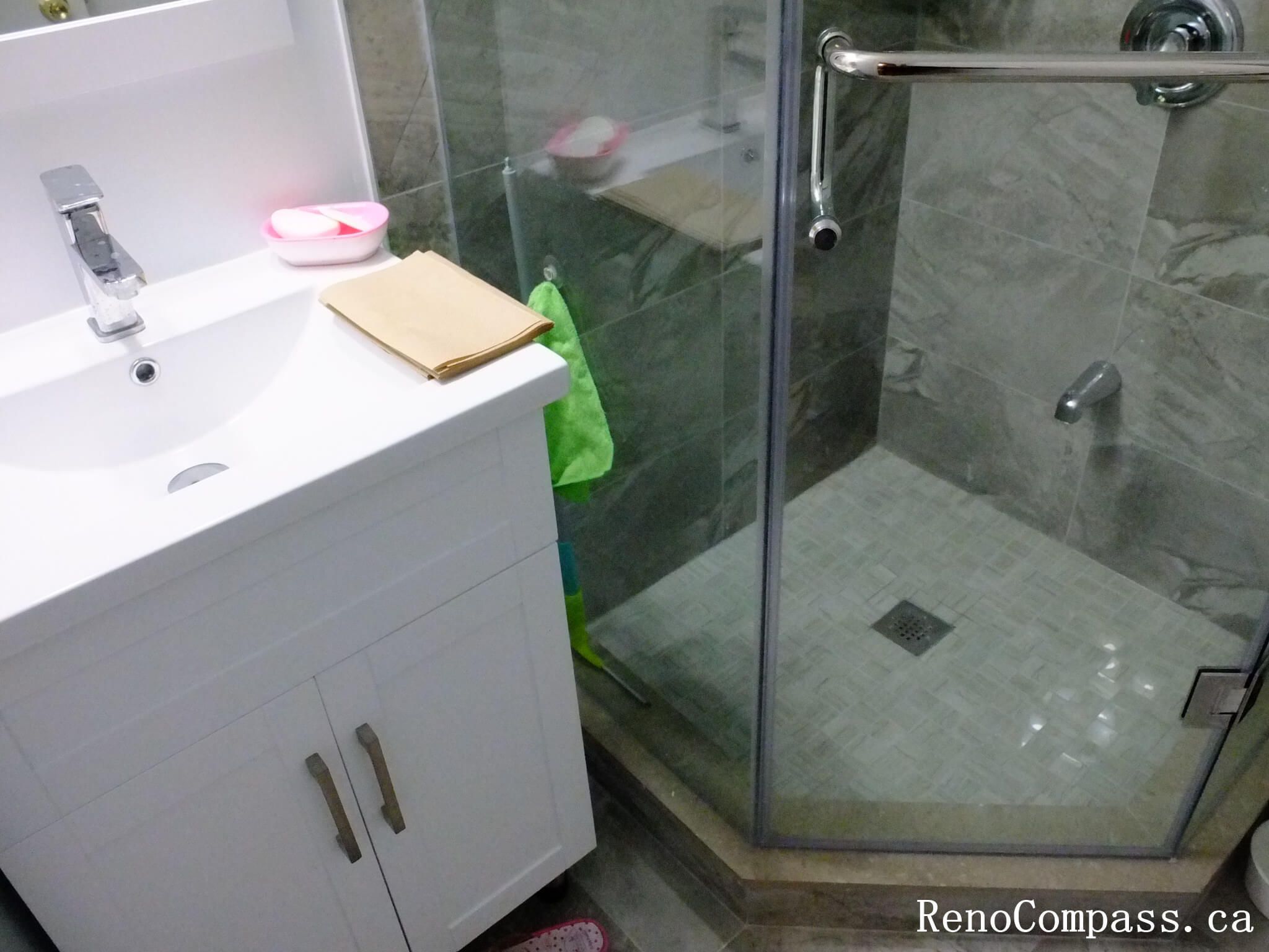 Bathroom renovation in North York showing the transition between the vanity area and a glass-enclosed shower, featuring a tiled shower floor with center drain and compact space planning. This Toronto interior renovation emphasizes functional layout, water management, and efficient use of bathroom space.