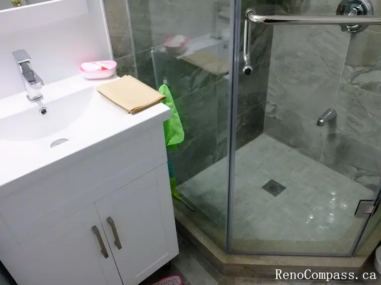 Bathroom renovation in North York showing the transition between the vanity area and a glass-enclosed shower, featuring a tiled shower floor with center drain and compact space planning. This Toronto interior renovation emphasizes functional layout, water management, and efficient use of bathroom space.