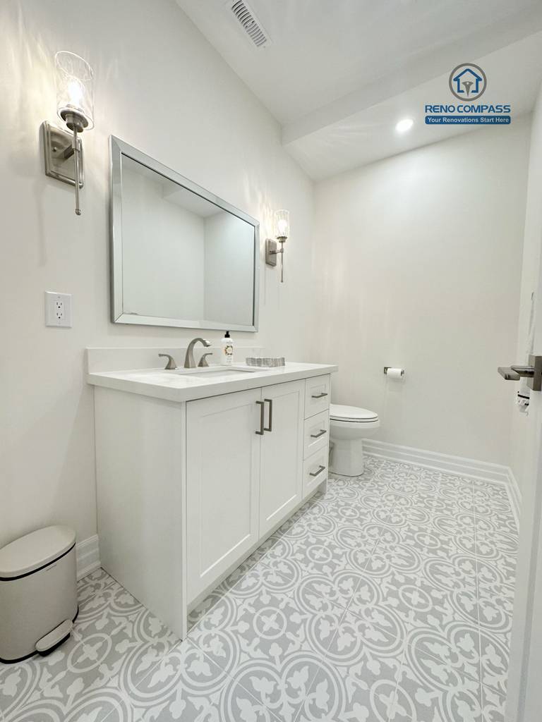 This Bradford basement renovation features a bright open-concept layout that combines a comfortable living area with a functional kitchenette. Custom white cabinetry, quartz countertops, and integrated seating create a clean and practical space for daily use and entertaining. Recessed ceiling lighting and wide-plank flooring enhance the sense of openness, while thoughtful column placement maintains structural clarity. Designed and built by a Toronto renovation company, this basement transformation adds valuable living space while maintaining a seamless connection to the home’s main design style.