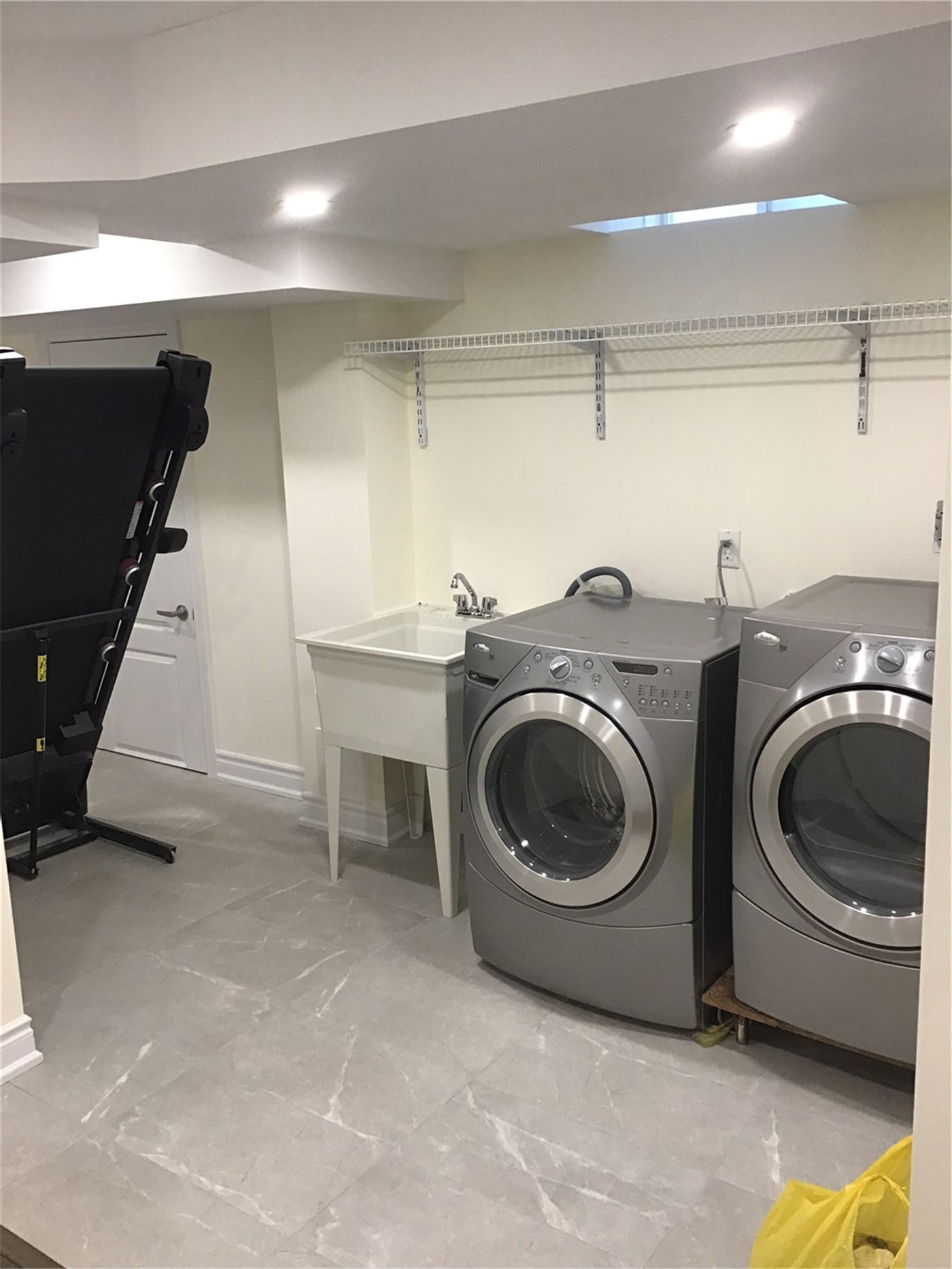 This Mississauga basement renovation includes a functional laundry room equipped with modern front-load washer and dryer, a utility sink, and ample storage space. The clean tile flooring and bright lighting create a practical and efficient environment for everyday use.