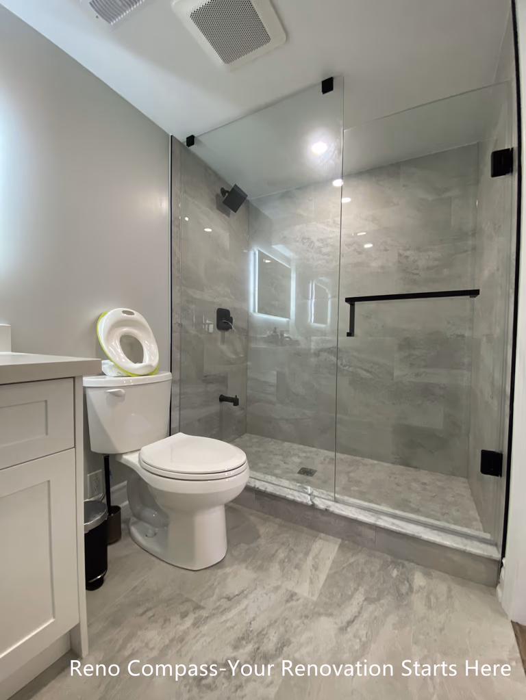 Full view of a modern basement bathroom renovation in Oakville featuring a frameless glass walk-in shower, marble-look tile flooring and walls, matte black shower hardware, efficient ventilation, and a clean, space-saving layout designed for basement living, completed by Reno Compass Inc.