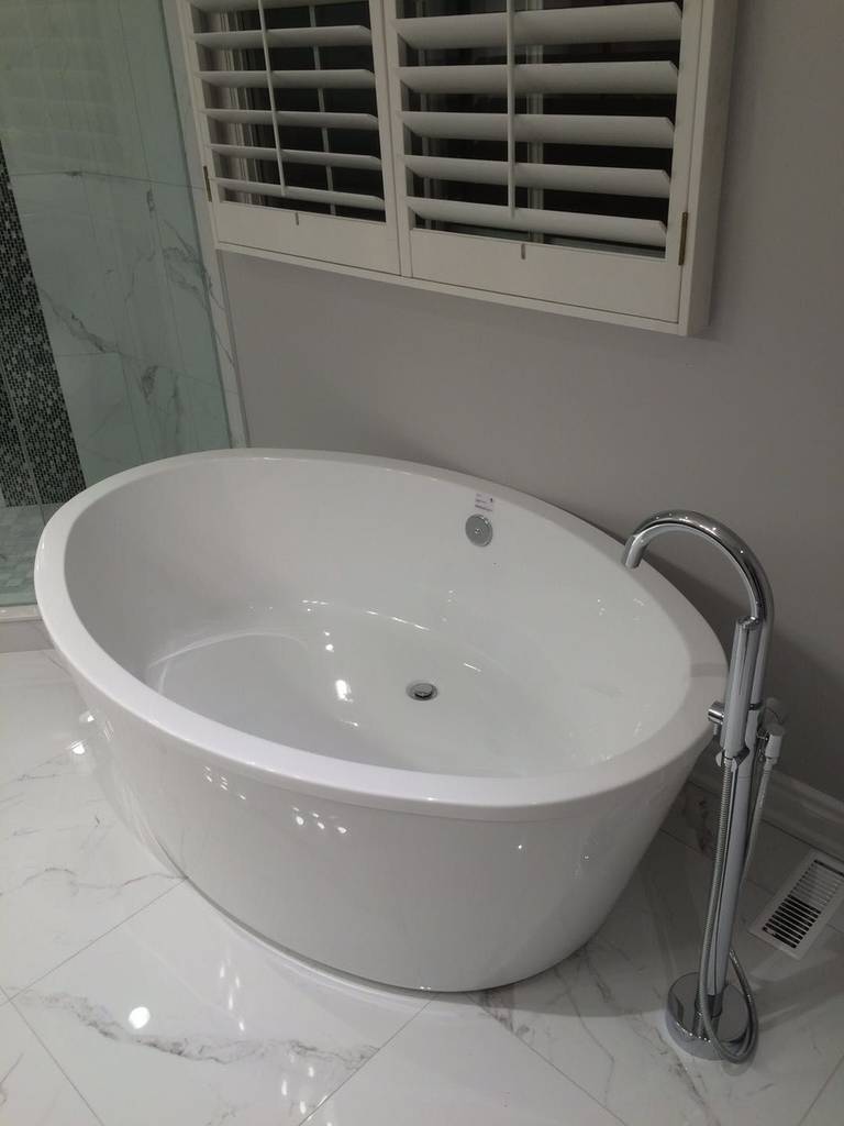 This Toronto bathroom renovation features a modern freestanding bathtub paired with a sleek floor-mounted faucet, creating a clean and luxurious spa-like atmosphere. Marble-style floor tiles and minimalist finishes enhance the sense of space and elegance. The upgraded bathtub area improves both comfort and visual appeal, offering a refined and relaxing bathing experience in a contemporary home.