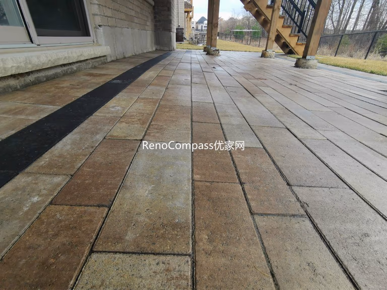 Professional interlocking patio installation in Aurora featuring durable stone pavers and clean border detailing beneath an elevated deck. This custom outdoor renovation improves drainage, usability, and backyard aesthetics while creating a functional covered patio space for all-season outdoor living.