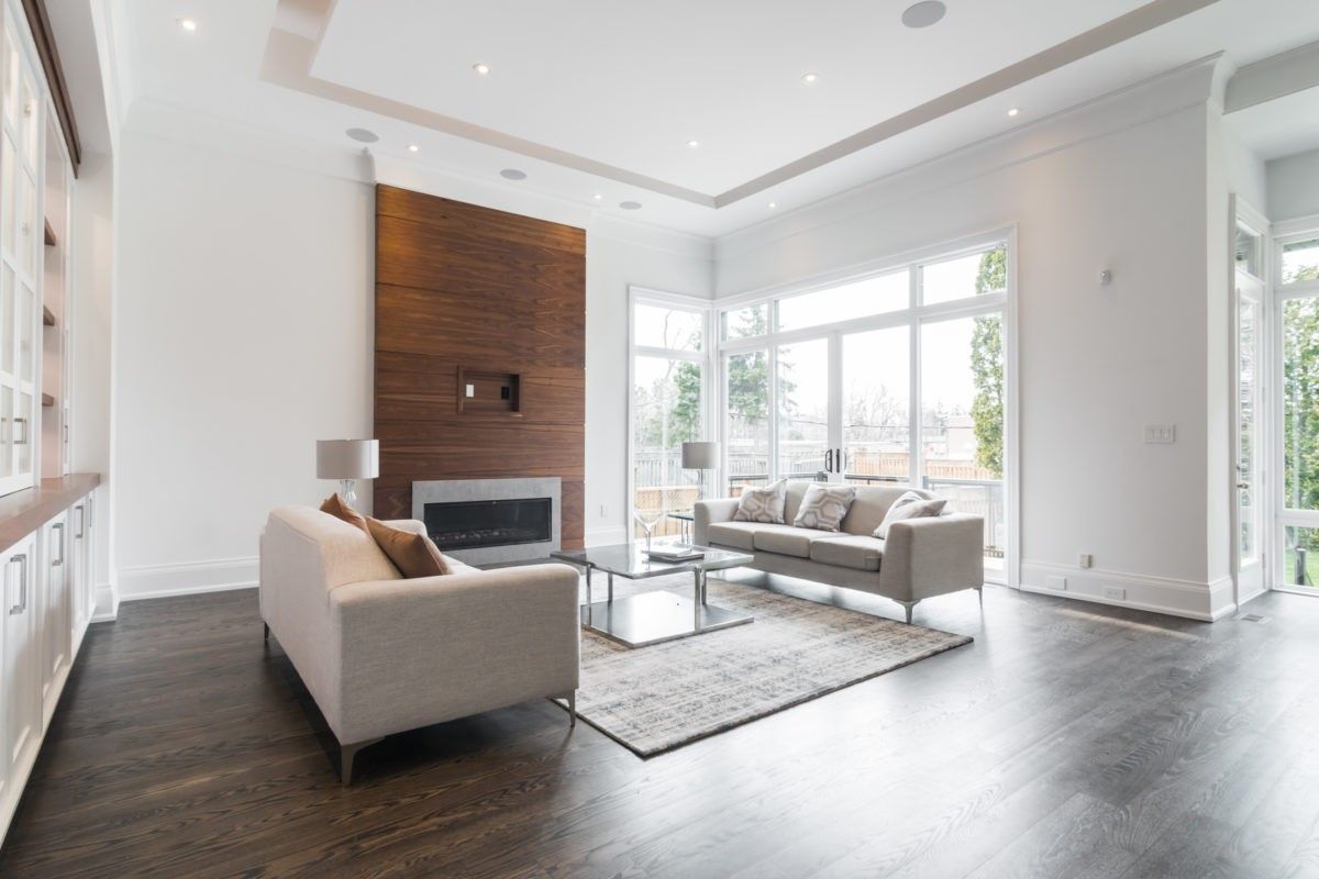 This 4,500 sq ft modern interior renovation in Toronto showcases a bright and expansive living room with floor-to-ceiling windows, a custom wood-paneled fireplace feature wall, and an elegant open-concept layout. The combination of dark hardwood flooring and soft neutral furnishings creates a refined yet inviting atmosphere. Designed and built by a trusted Toronto Renovation Company, Reno Compass Inc., this project reflects premium craftsmanship and sophisticated contemporary living.