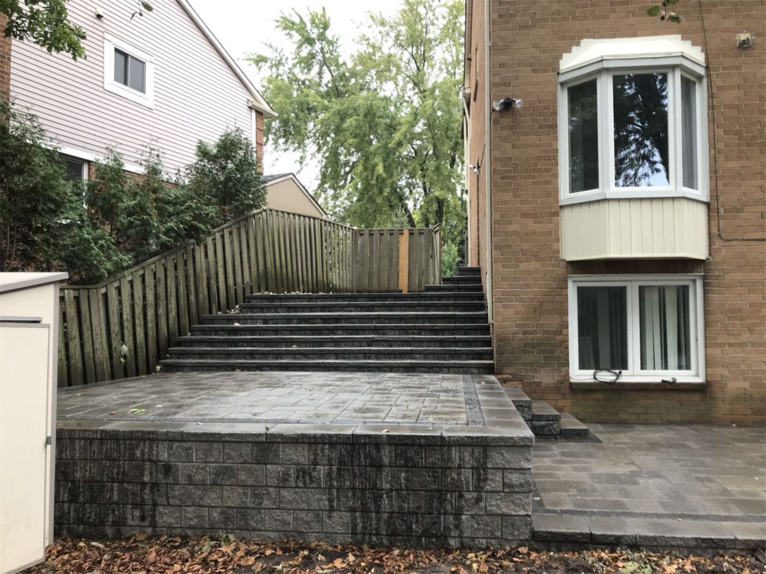 Backyard landscaping renovation in Toronto featuring a raised stone terrace, retaining wall structure, and wide landscape steps leading to the upper garden area. The design improves backyard accessibility while creating a clean and durable outdoor living space.