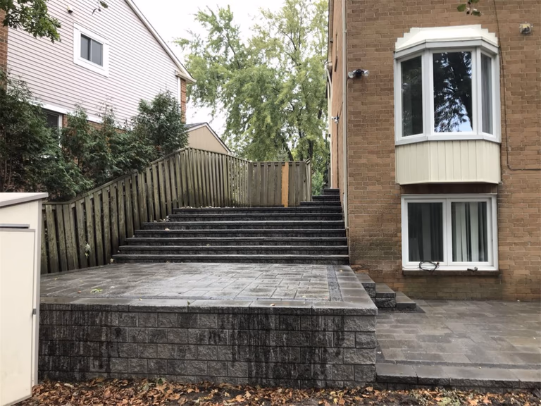 Backyard landscaping renovation in Toronto featuring a raised stone terrace, retaining wall structure, and wide landscape steps leading to the upper garden area. The design improves backyard accessibility while creating a clean and durable outdoor living space.
