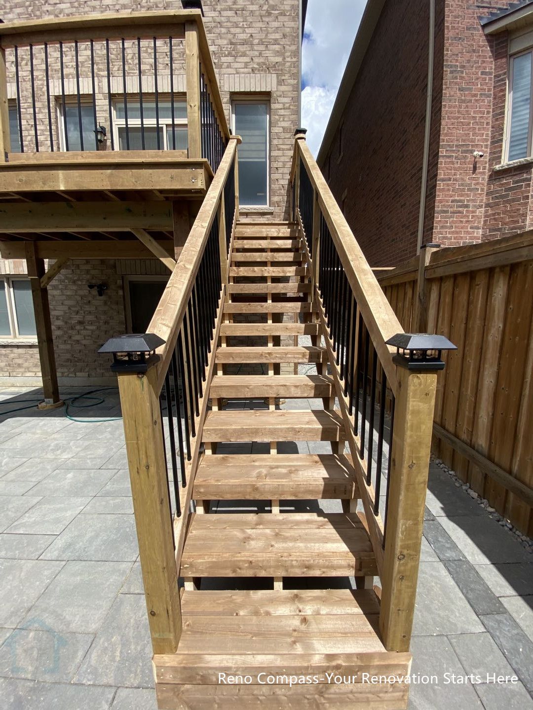 This image highlights the custom-built wooden staircase designed to connect the raised deck with the interlocking stone patio in this Markham backyard renovation. The staircase features pressure-treated wood steps and clean black metal railings, providing both structural stability and visual contrast. Even spacing and clear sightlines improve safety and everyday usability, while integrated post cap lighting enhances visibility during evening use. The staircase serves as a functional transition between outdoor levels, reinforcing circulation flow and long-term durability. This outdoor deck and stair construction was completed by Reno Compass, serving homeowners in Markham and across the GTA.