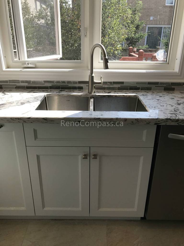 Light grey custom kitchen cabinets with decorative glass inserts and granite countertops under a bright window in a Markham home.