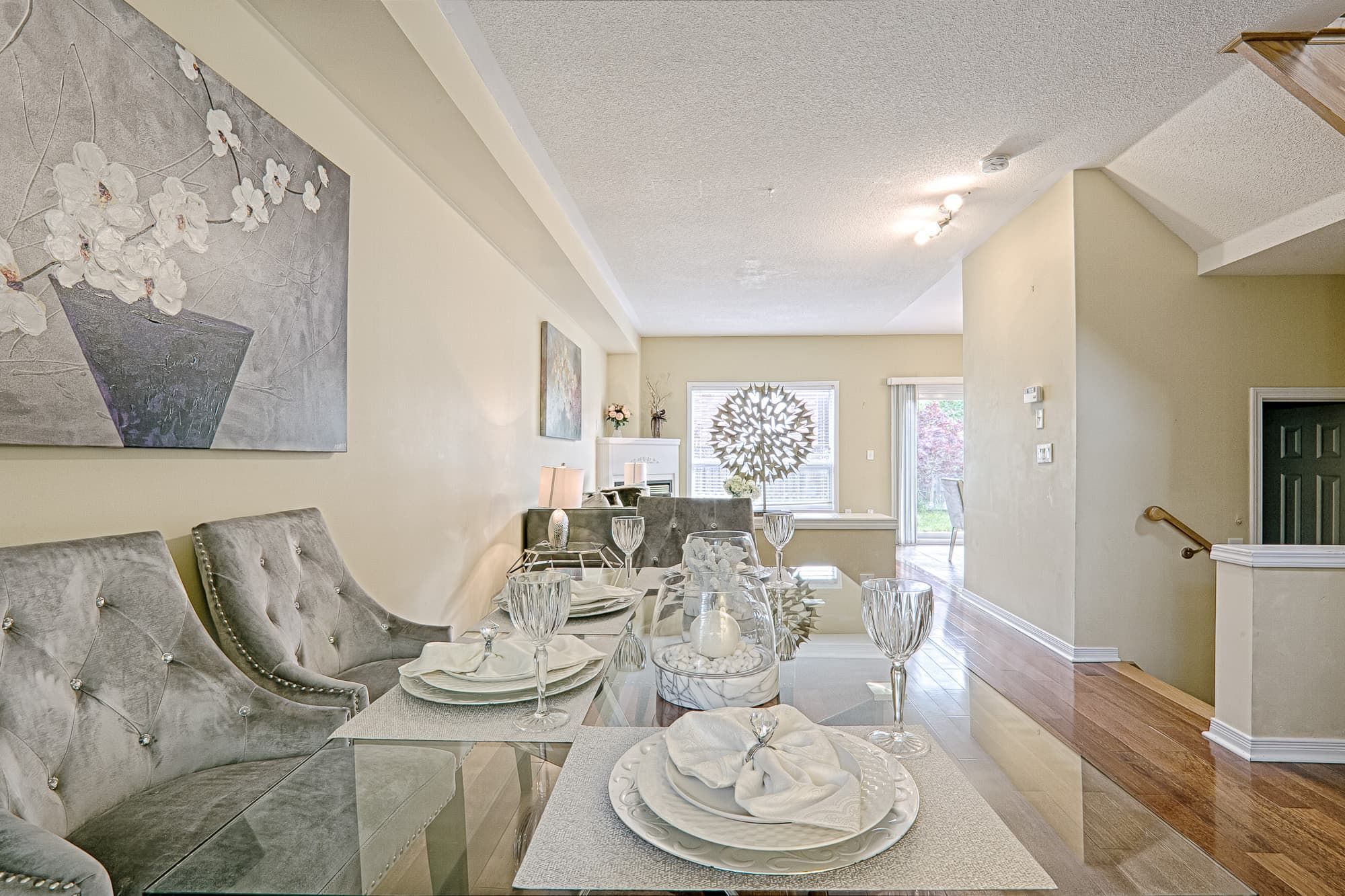 This elegant dining table setting highlights a simple and lovely interior design with a clean open layout and refined staging details. The glass tabletop, upholstered dining chairs, and neutral color palette create a light and sophisticated atmosphere. The long visual axis enhances depth and openness, making the space feel bright, balanced, and suitable for everyday dining and entertaining in modern family homes.