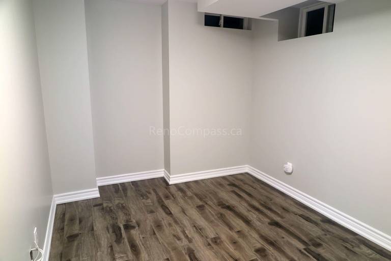 After photo from a Richmond Hill basement renovation project, featuring newly installed laminate flooring, fresh paint, and updated baseboards. The clean and bright design creates a comfortable, modern living or recreation area.