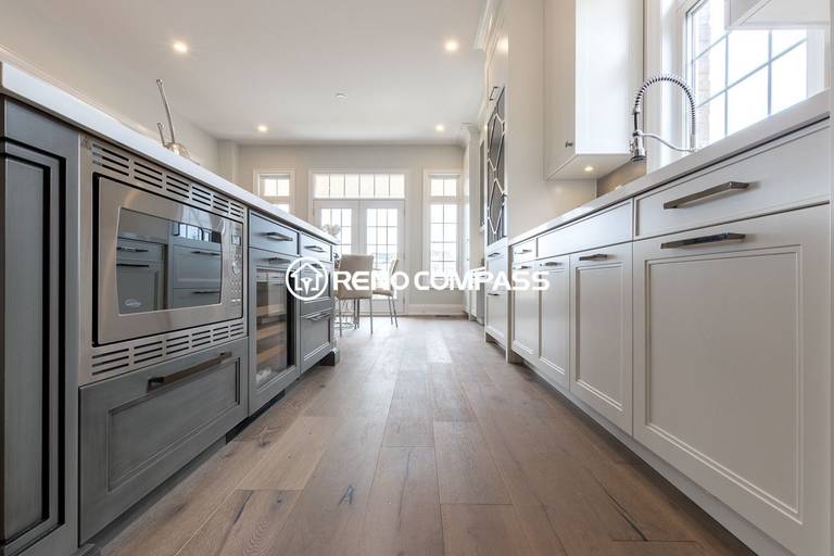 This Newmarket kitchen renovation highlights a spacious island with built-in appliances and custom white cabinetry. Engineered wood flooring and modern lighting create a bright and elegant open-concept kitchen layout that connects seamlessly to the dining area. Completed by a professional Toronto renovation company, Reno Compass Inc., the project demonstrates refined craftsmanship and functional kitchen design.