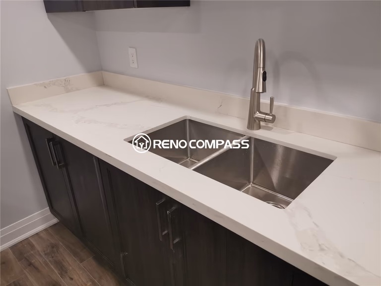 This Markham basement renovation highlights a modern kitchenette featuring a durable quartz countertop, stainless steel double sink, and custom dark wood base cabinetry. The clean countertop surface provides ample preparation space while maintaining a sleek, contemporary aesthetic suited for basement living or entertainment use. Designed for functionality and long-term durability, the materials are moisture-resistant and easy to maintain. Completed by a professional Toronto renovation company, this project showcases quality countertop installation, detailed cabinetry work, and practical basement remodeling solutions for homes across the Greater Toronto Area.