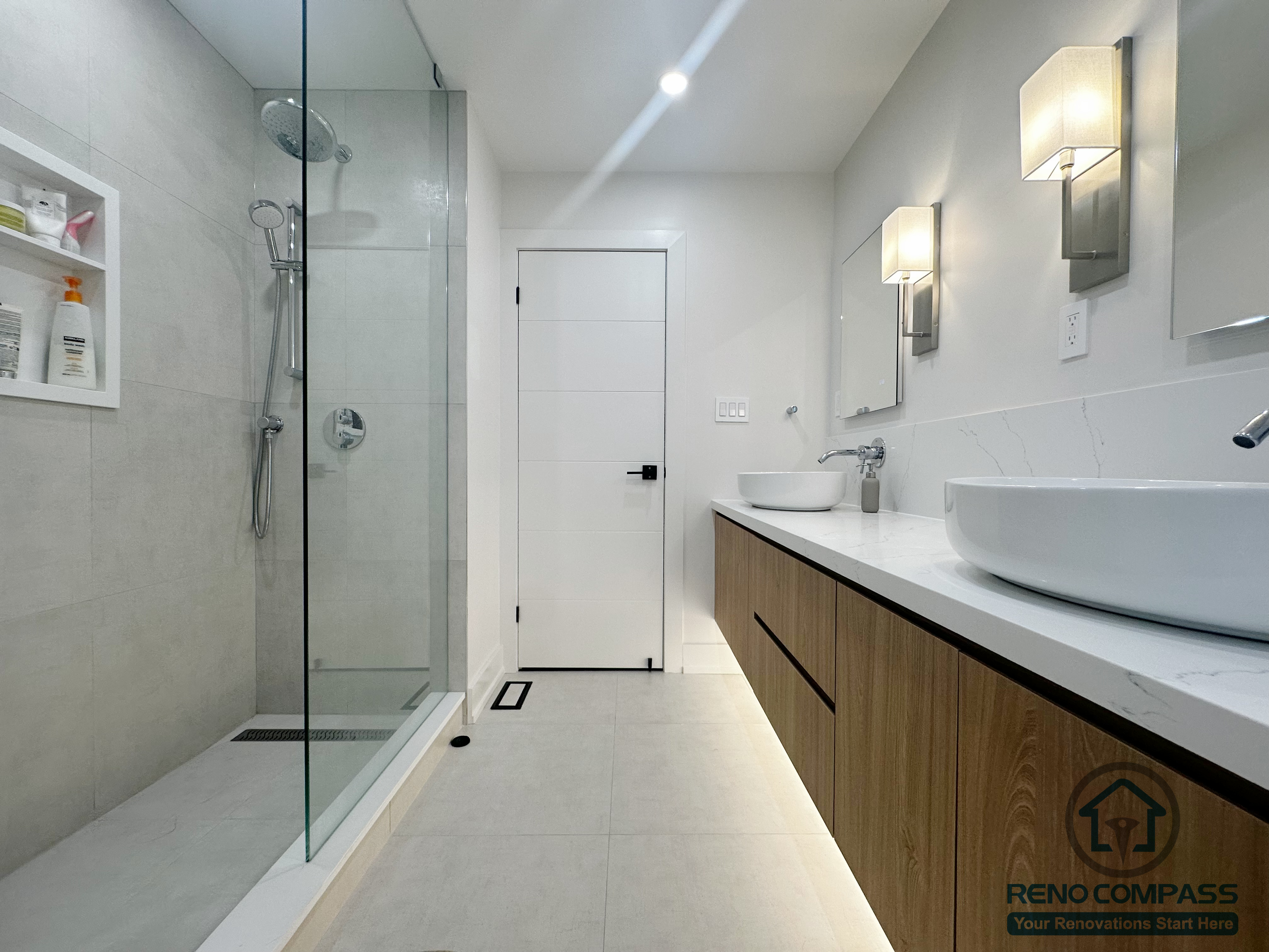 This Oakville bathroom renovation features a clean, modern layout with a frameless glass shower, large-format wall tiles, and a floating double vanity with integrated under-cabinet lighting. The design emphasizes simplicity and functionality, using neutral tones, wall-mounted fixtures, and a seamless glass enclosure to create a bright, spacious feel while maintaining a refined, contemporary aesthetic.