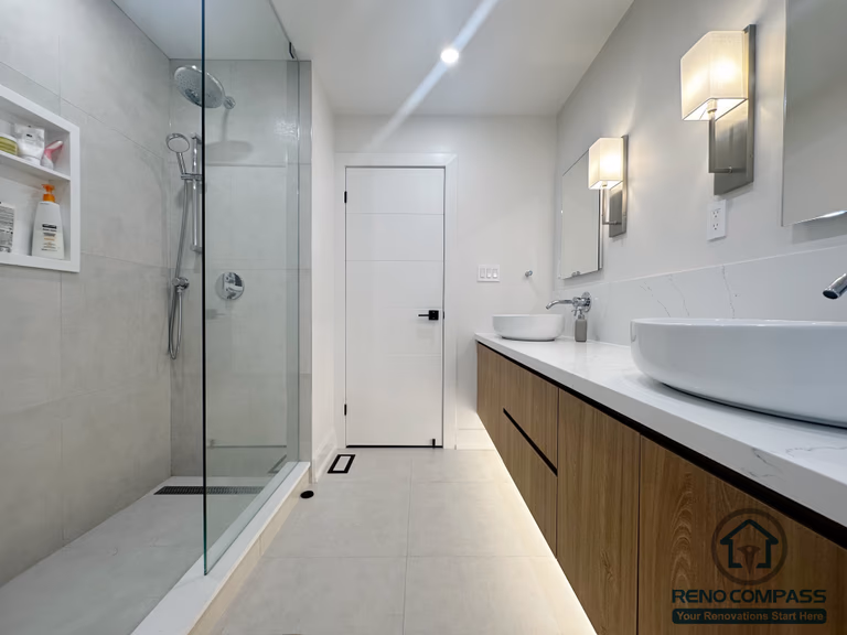 This Oakville bathroom renovation features a clean, modern layout with a frameless glass shower, large-format wall tiles, and a floating double vanity with integrated under-cabinet lighting. The design emphasizes simplicity and functionality, using neutral tones, wall-mounted fixtures, and a seamless glass enclosure to create a bright, spacious feel while maintaining a refined, contemporary aesthetic.