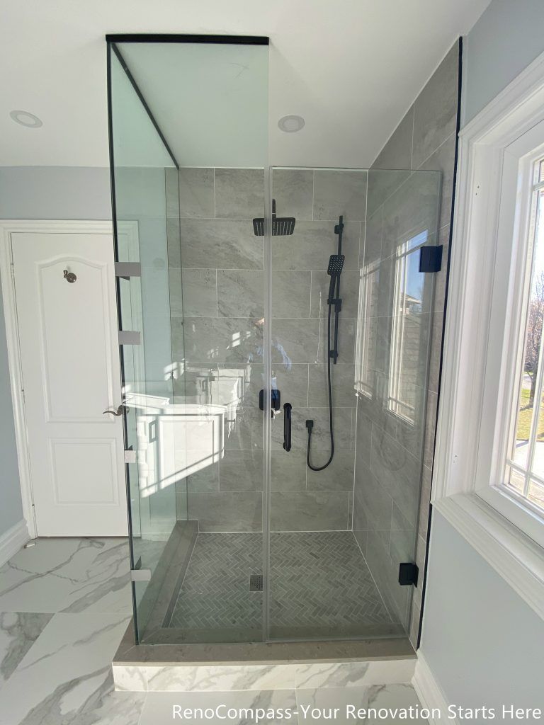 This Thornhill bathroom renovation features a modern walk-in shower enclosed with frameless glass panels, creating a bright and visually open space. The shower is finished with large-format gray wall tiles, a patterned shower base, and matte black fixtures for a clean, contemporary contrast. Natural light from the window enhances the overall brightness, while the glass enclosure replaces traditional drywall to significantly improve spatial flow, functionality, and long-term usability.