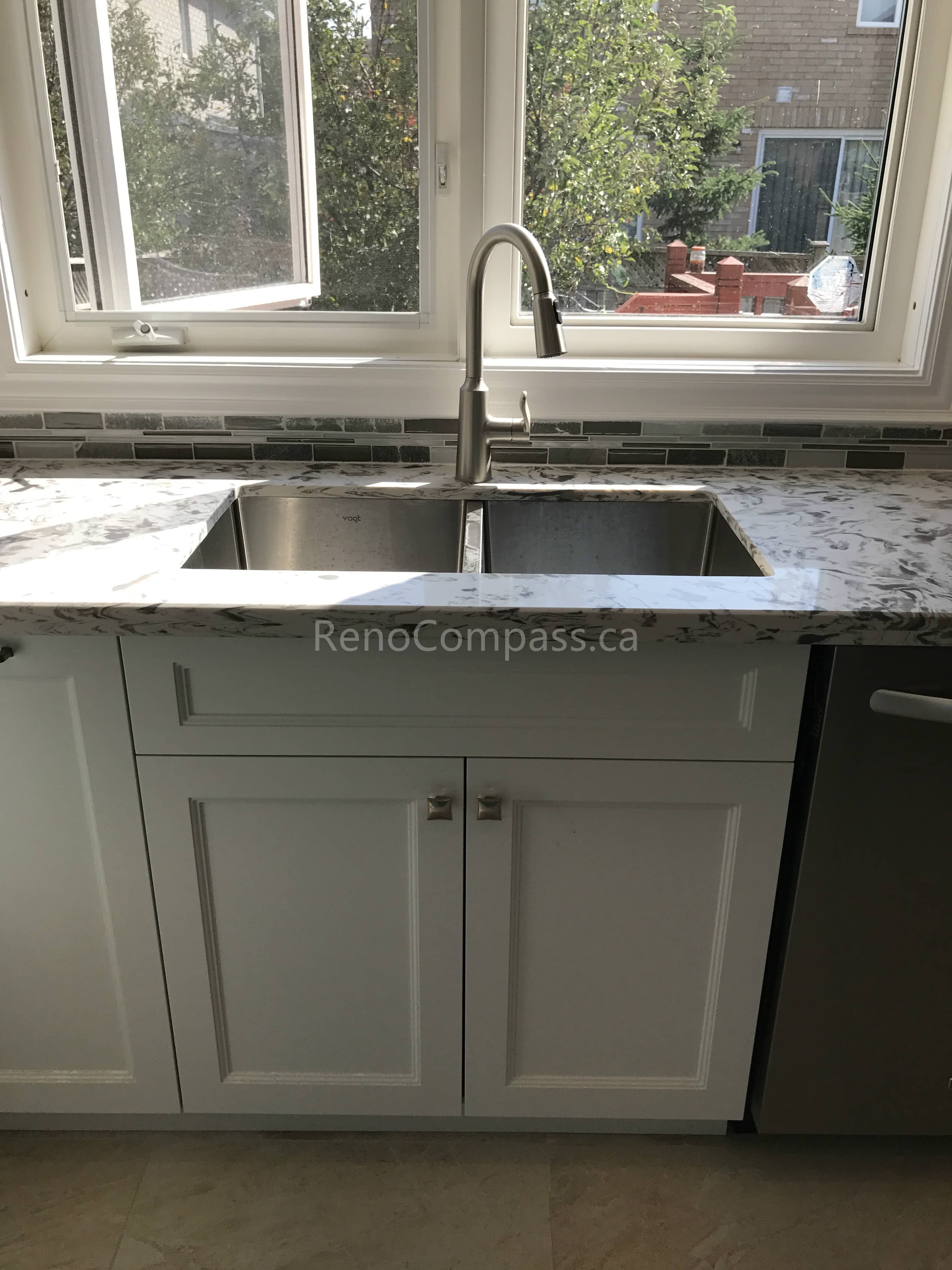 This Markham kitchen renovation features a modern double-bowl stainless steel sink set beneath a large window for enhanced natural light. Paired with granite countertops, custom white cabinetry, and a sleek mosaic tile backsplash, the design combines everyday functionality with a clean, timeless aesthetic suited for modern family living.