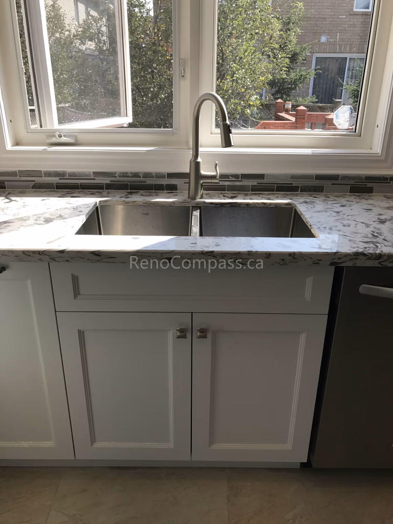 This Markham kitchen renovation features a modern double-bowl stainless steel sink set beneath a large window for enhanced natural light. Paired with granite countertops, custom white cabinetry, and a sleek mosaic tile backsplash, the design combines everyday functionality with a clean, timeless aesthetic suited for modern family living.