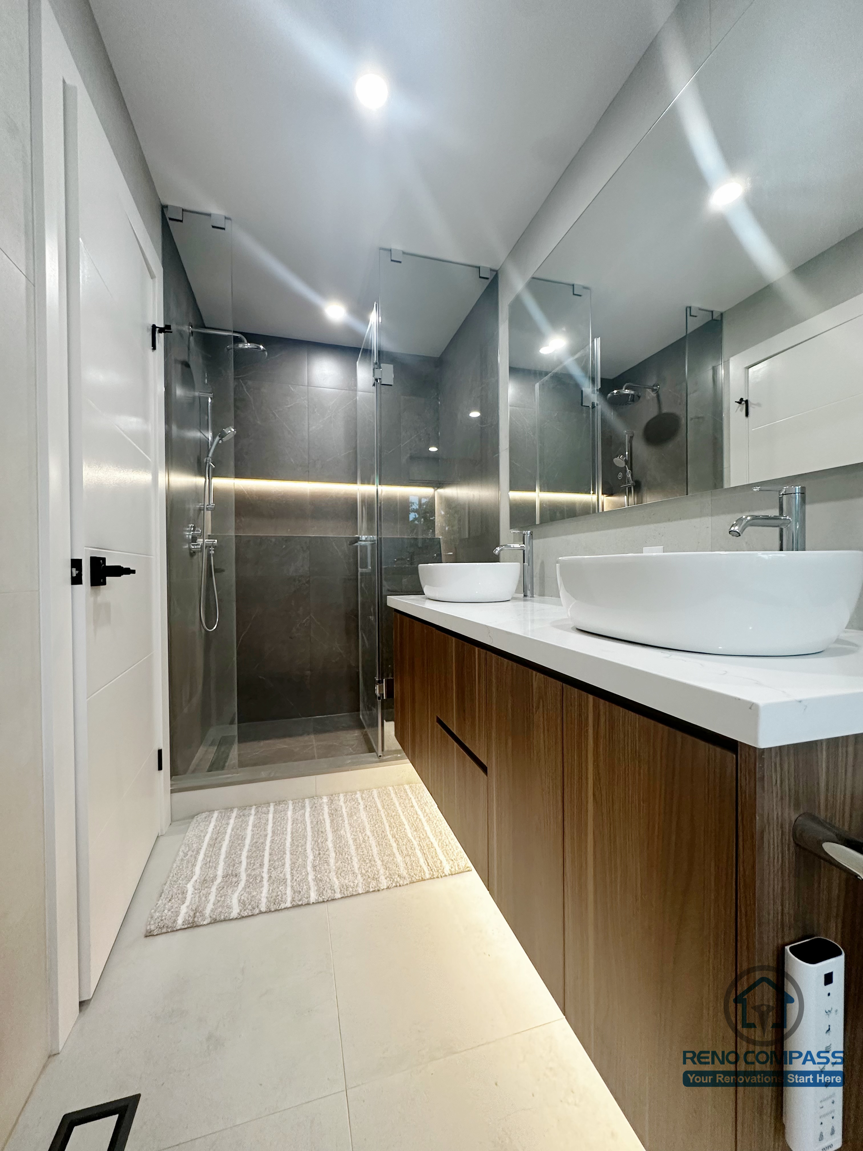 This Oakville bathroom renovation features a sleek walk-in glass shower paired with a floating wood vanity and vessel sinks. Neutral tile finishes, integrated lighting, and clean-lined fixtures create a calm, modern atmosphere while enhancing daily functionality and visual balance throughout the space.