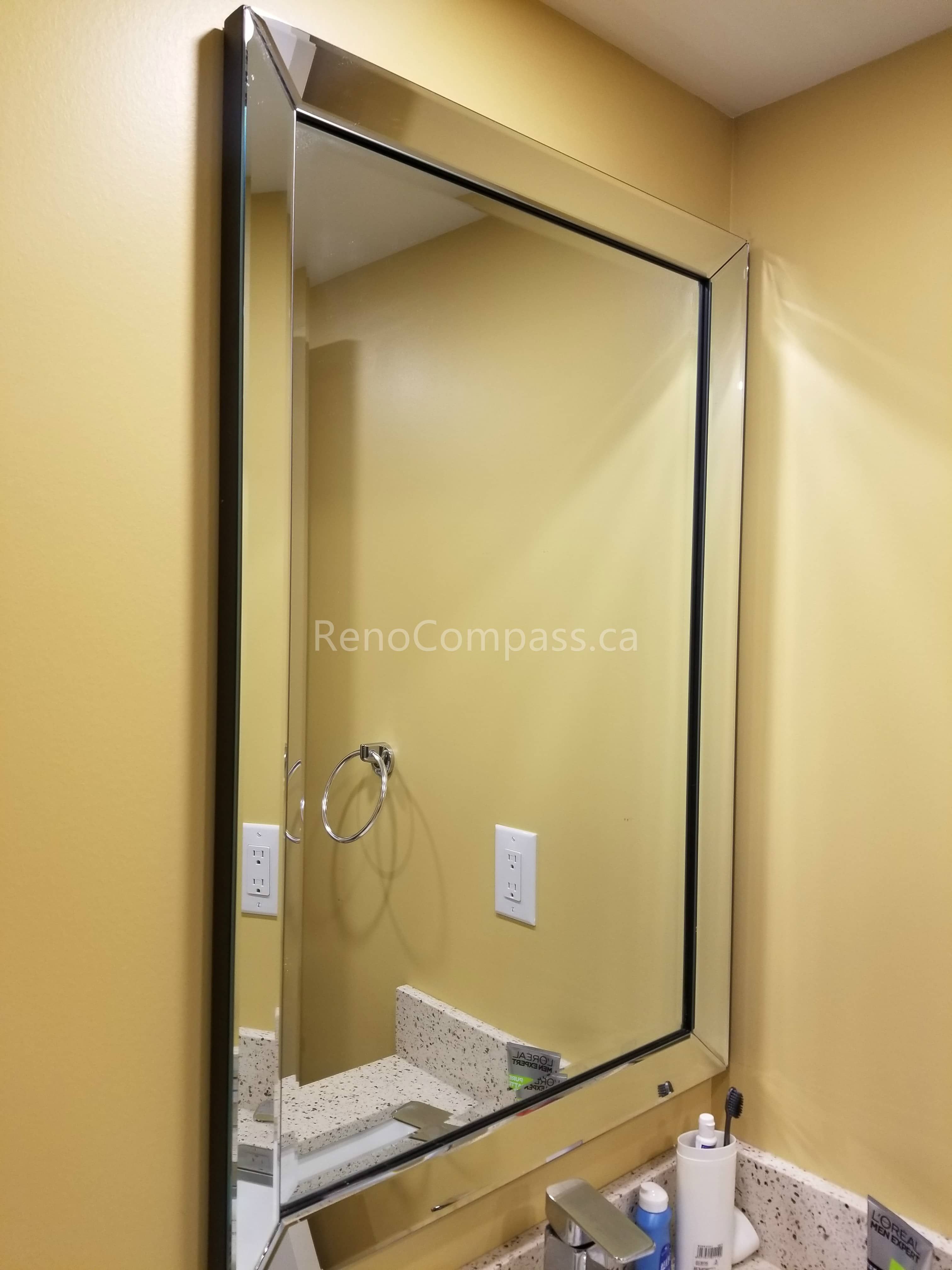 This Vaughan basement renovation features a clean and modern bathroom upgrade with a sleek framed vanity mirror and updated sink area. The bright wall color, stone countertop, and refined mirror installation enhance lighting reflection and create a more spacious, functional bathroom environment. Completed by Reno Compass Inc., this basement bathroom improvement adds both style and practicality to the finished living space.