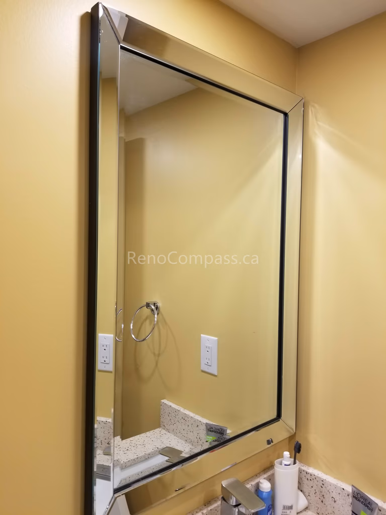 This Vaughan basement renovation features a clean and modern bathroom upgrade with a sleek framed vanity mirror and updated sink area. The bright wall color, stone countertop, and refined mirror installation enhance lighting reflection and create a more spacious, functional bathroom environment. Completed by Reno Compass Inc., this basement bathroom improvement adds both style and practicality to the finished living space.
