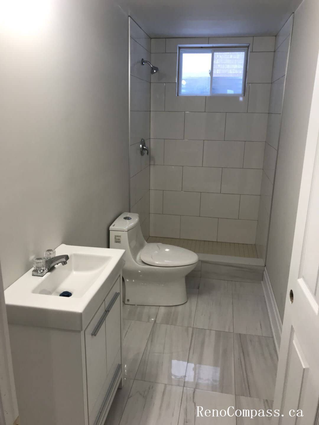 This Markham interior renovation includes a fully upgraded bathroom featuring a clean and modern layout. The space showcases large-format light gray porcelain floor tiles, a sleek white vanity with integrated sink, and a tiled walk-in shower with a built-in window for natural light. The neutral color palette enhances brightness while maintaining a contemporary and low-maintenance design. Carefully executed plumbing fixtures and tile alignment reflect Reno Compass’ commitment to precision craftsmanship and high-quality interior renovation services in Markham and the Greater Toronto Area.