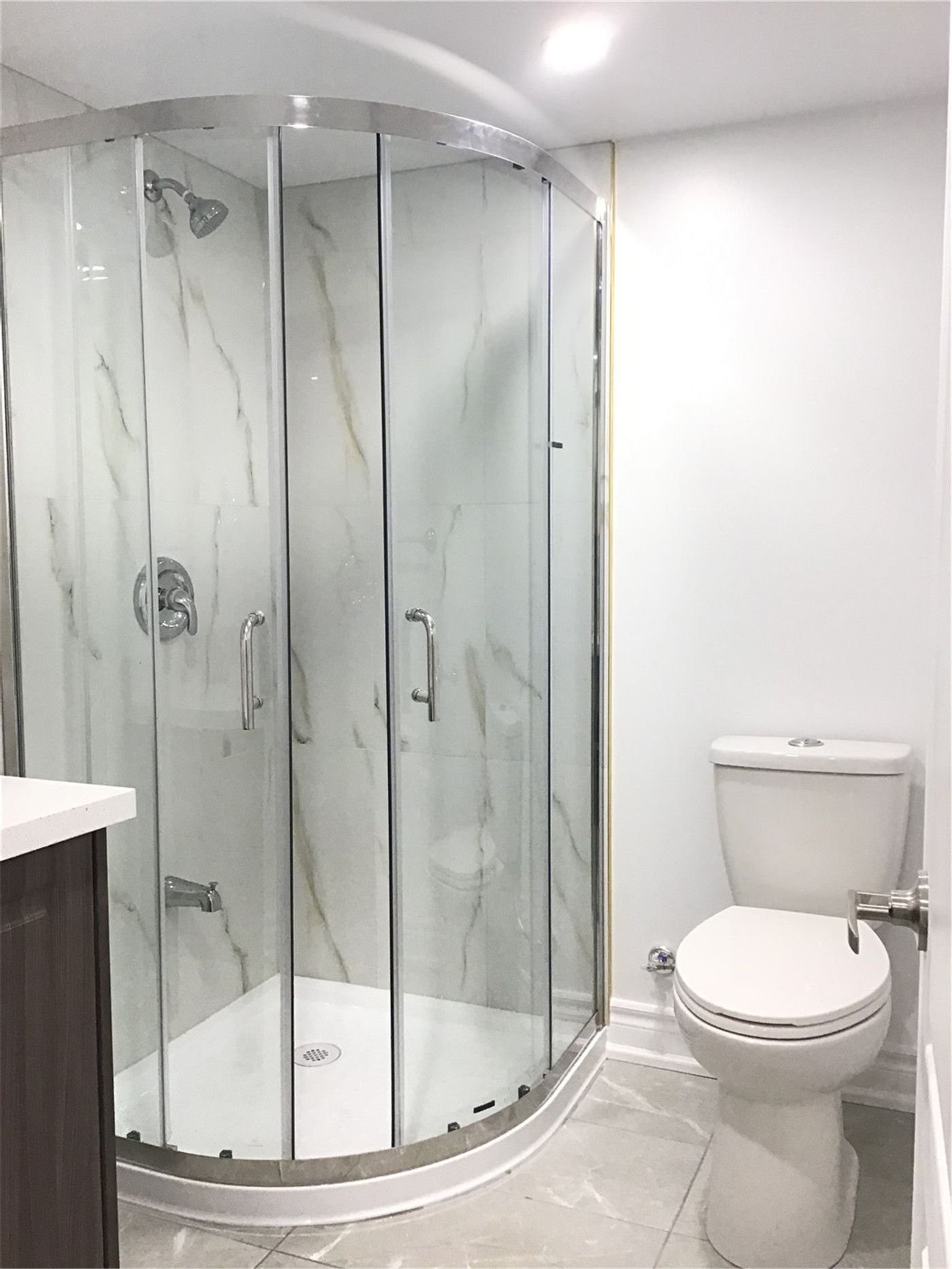 This Mississauga basement bathroom renovation features a modern curved glass shower enclosure with marble-style wall panels, paired with a compact vanity and upgraded fixtures. Completed by a professional Toronto Renovation Company, the design maximizes functionality in a small basement bathroom while maintaining a clean, bright, and contemporary look—ideal for a finished basement or rental suite.