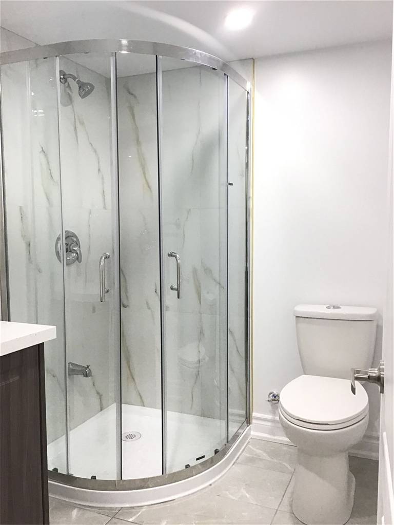 This Mississauga basement bathroom renovation features a modern curved glass shower enclosure with marble-style wall panels, paired with a compact vanity and upgraded fixtures. Completed by a professional Toronto Renovation Company, the design maximizes functionality in a small basement bathroom while maintaining a clean, bright, and contemporary look—ideal for a finished basement or rental suite.