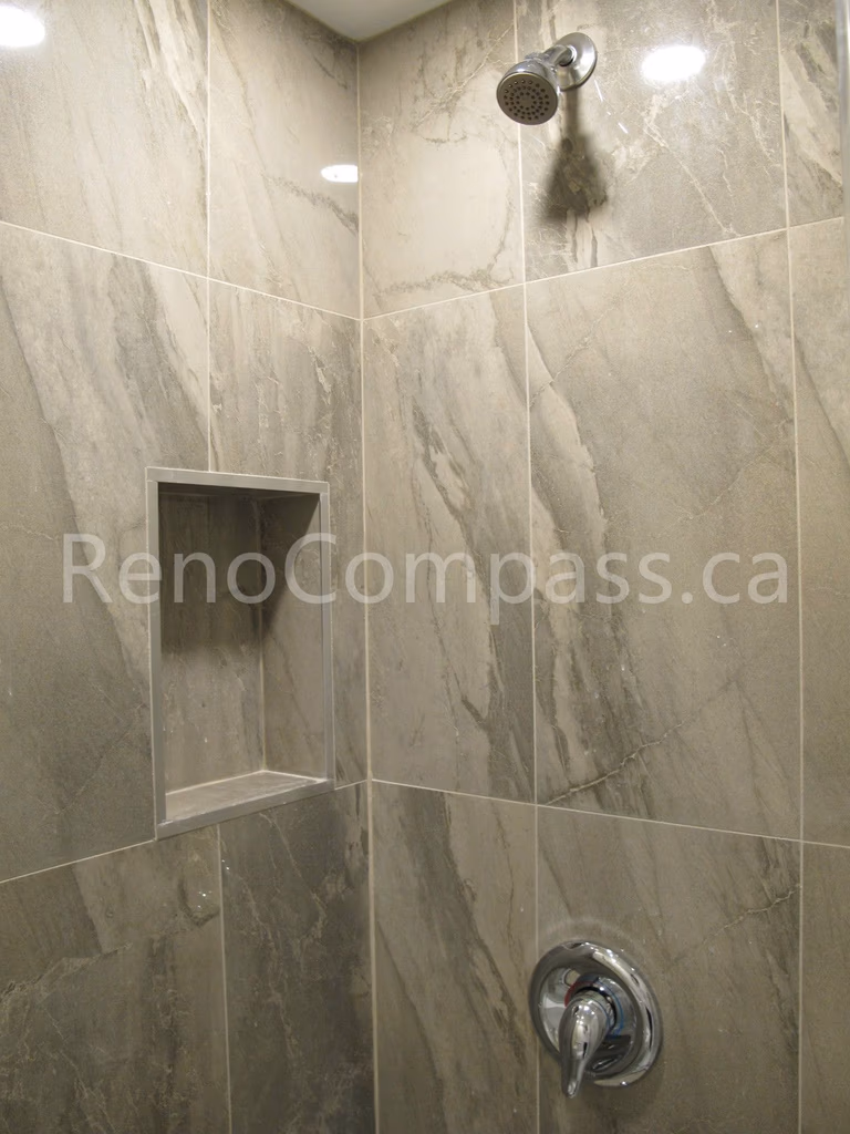 Close-up of custom shower tile installation in this Markham basement renovation, featuring marble-look porcelain tiles, recessed storage niche, and modern chrome fixtures. Completed by Reno Compass, this bathroom detail showcases precise tile work and functional design for a stylish and durable basement shower space.